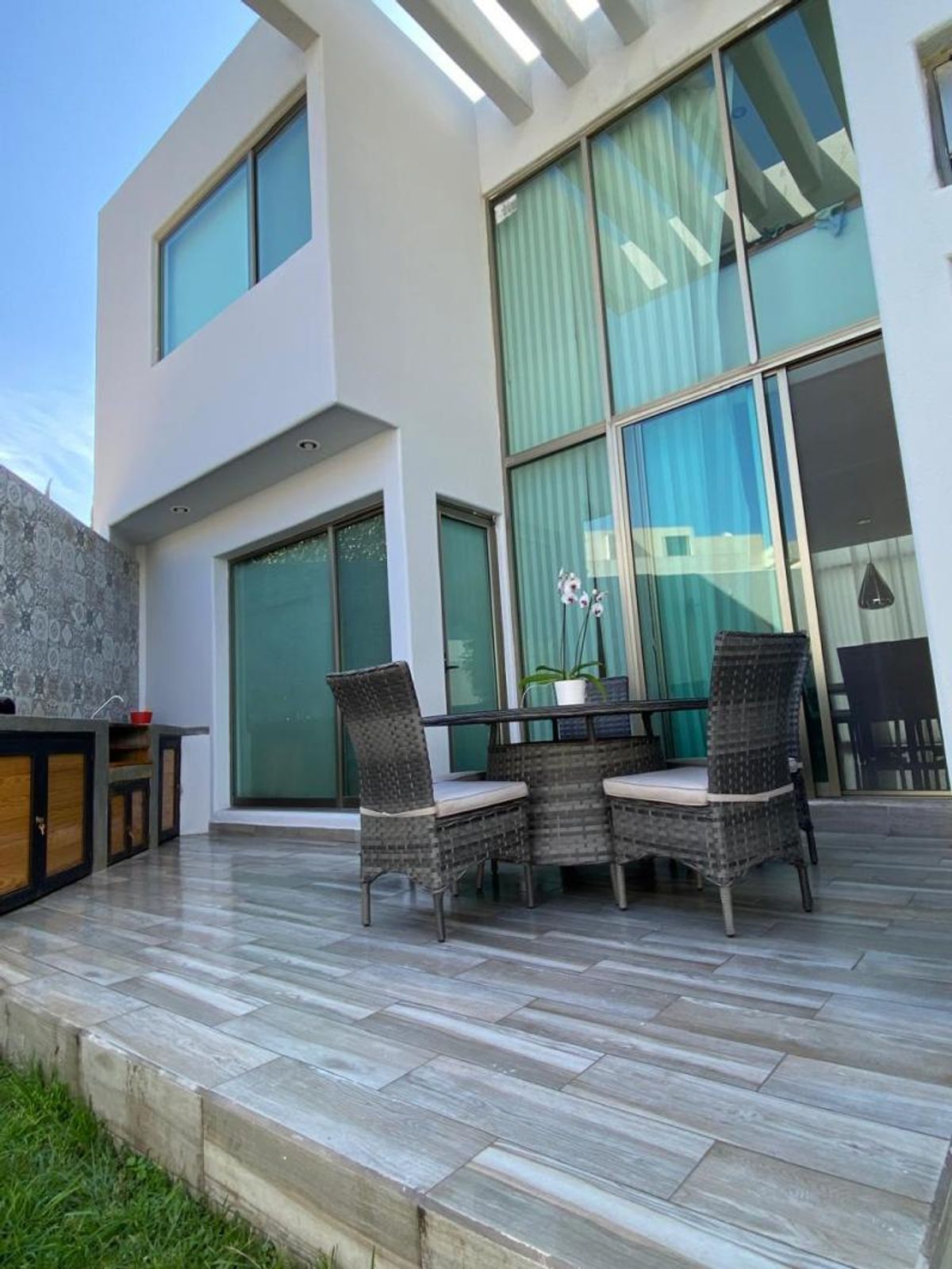 Terraza con piso cerámico tipo madera, comedor exterior de mimbre y grandes ventanales