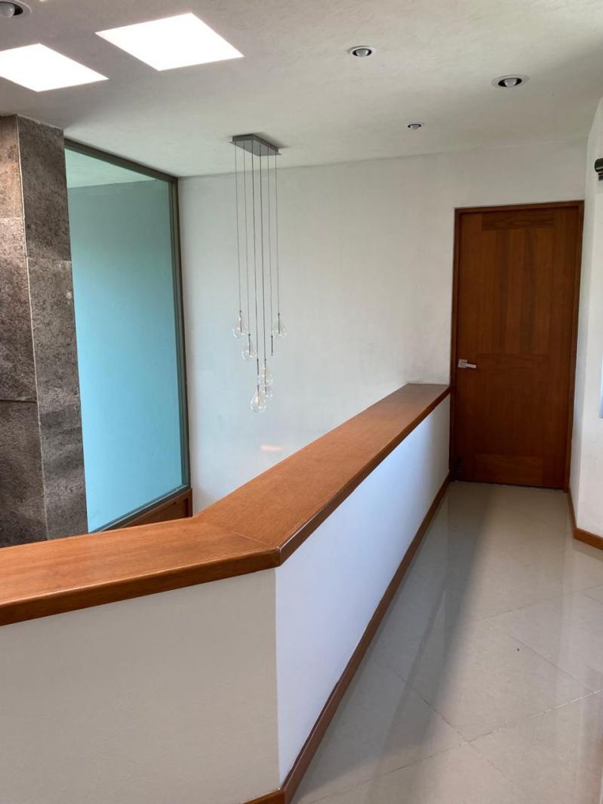 Pasillo con pasamanos de madera, lámpara colgante de cristal y puerta al fondo