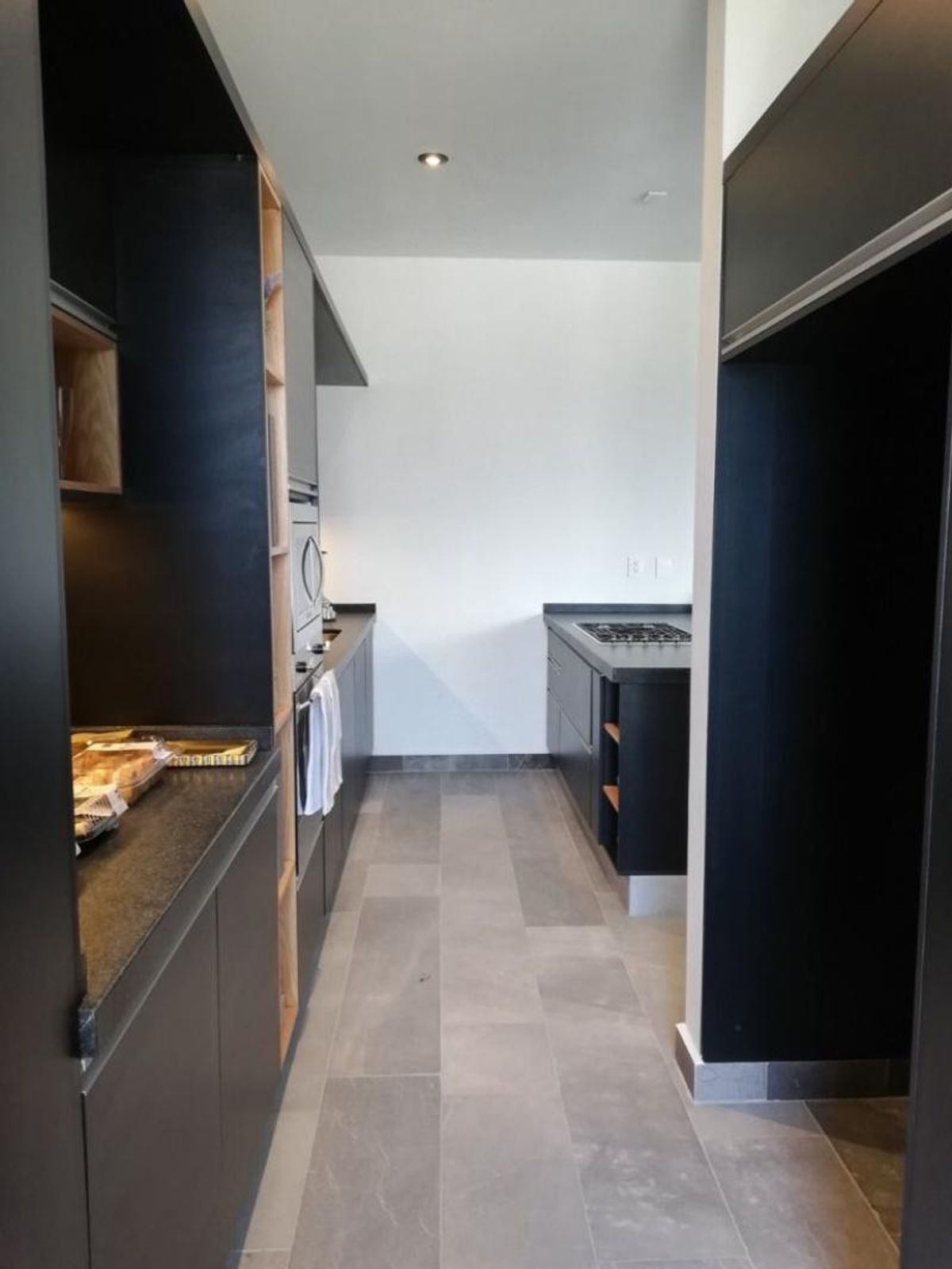 Cocina moderna tipo pasillo con muebles negros, cubierta oscura y piso gris