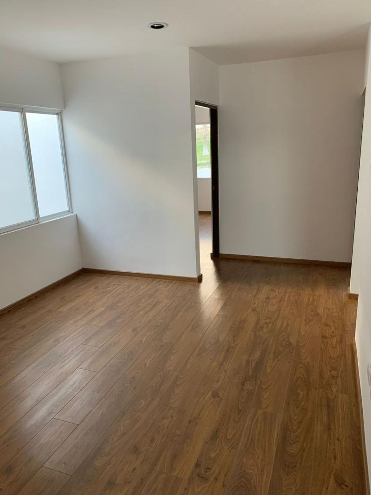Habitación vacía con piso de madera laminada, paredes blancas y ventana con cristal opaco