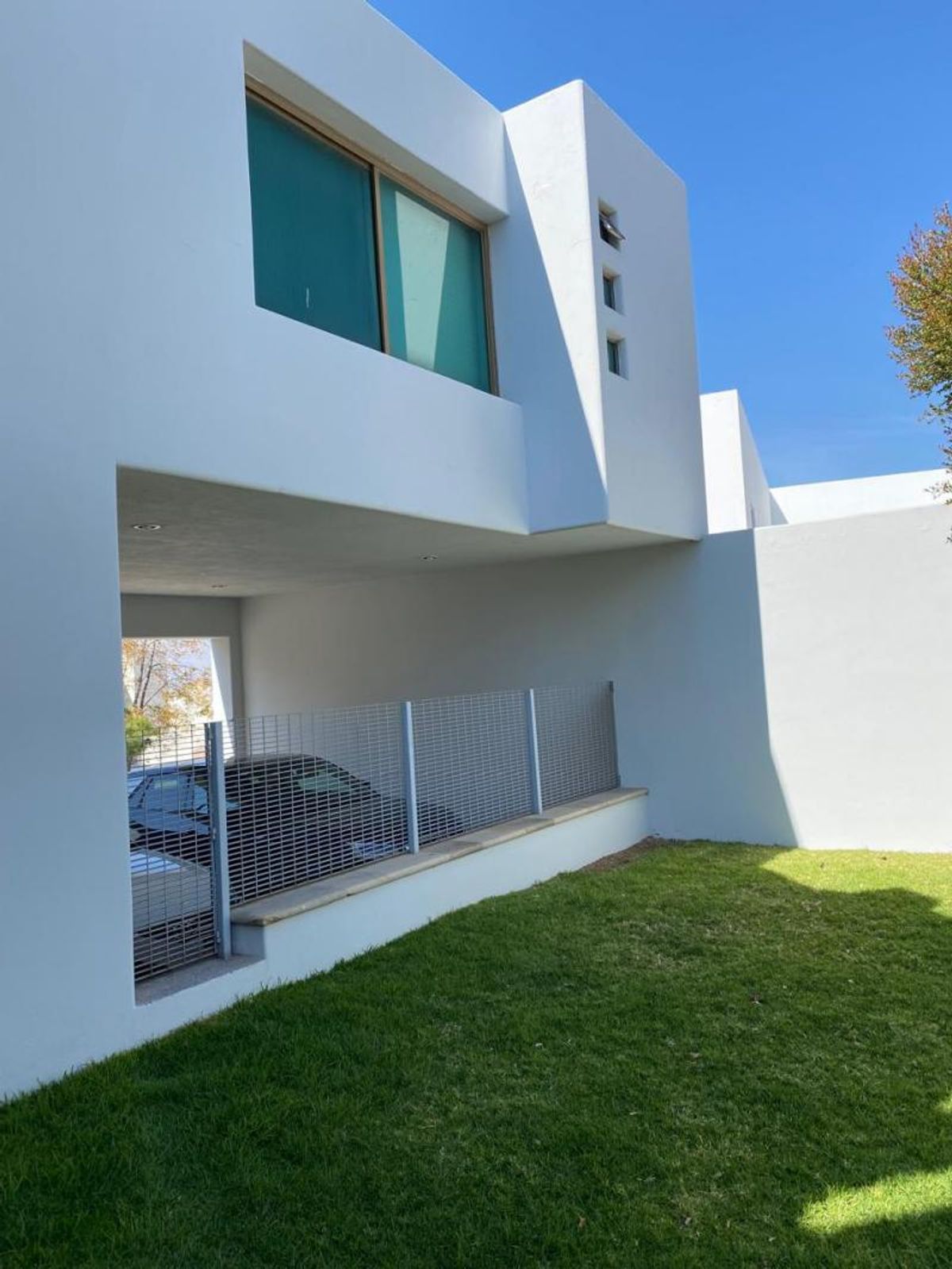 Fachada blanca de estilo moderno con patio de césped verde y cochera cubierta