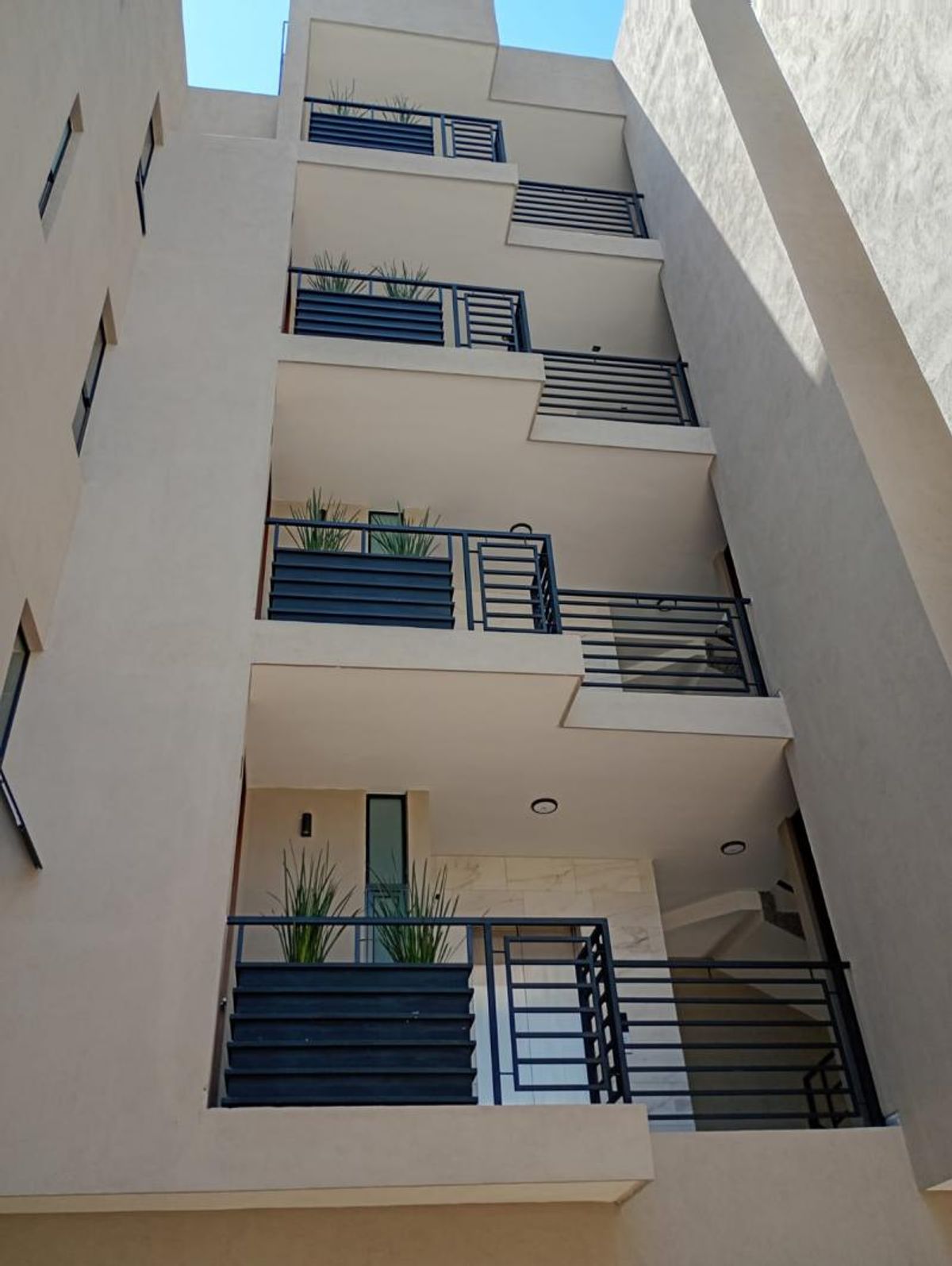 Fachada de edificio residencial con balcones de barandales metálicos negros y jardineras con plantas