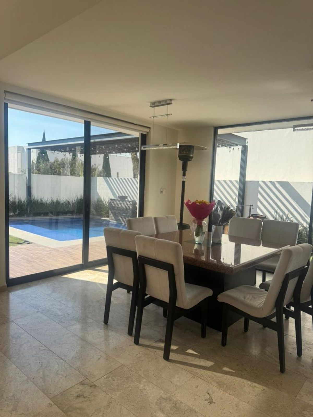 Comedor con piso claro, mesa grande, sillas tapizadas y ventanales hacia la alberca