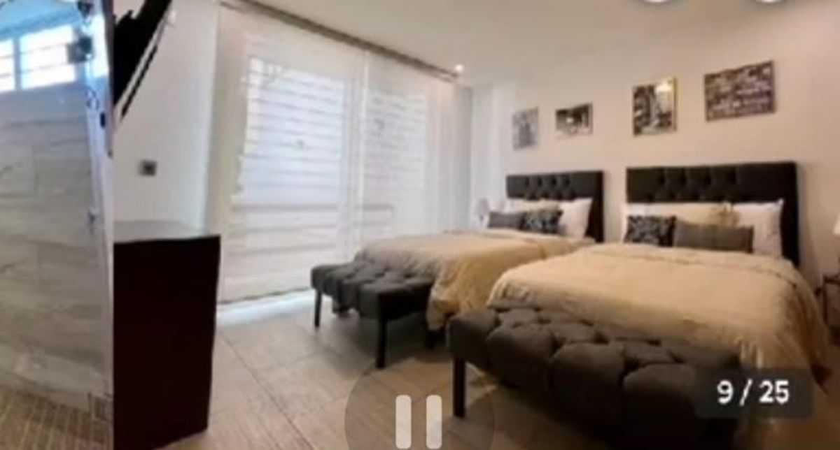 Recámara con dos camas, cabeceras tapizadas oscuras, bancos al pie y persianas en ventanal