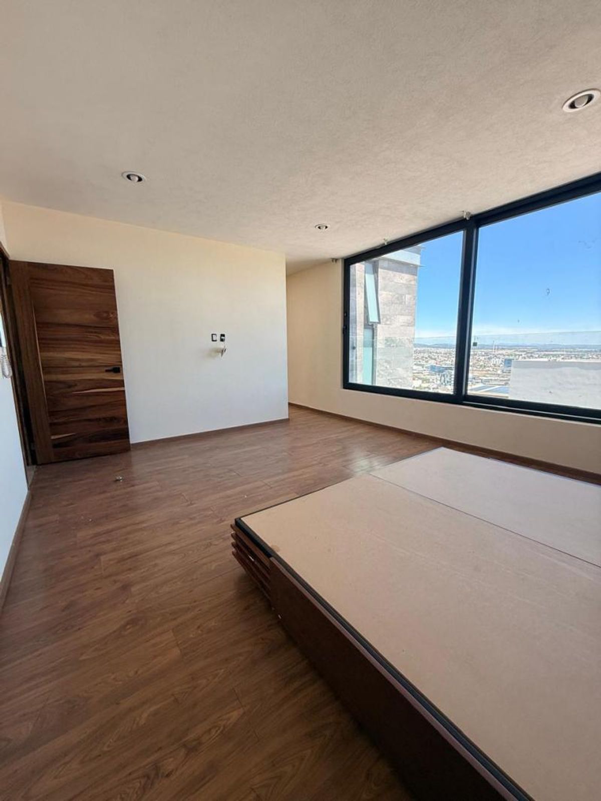 Recámara con piso de madera, base de cama de madera y gran ventanal panorámico