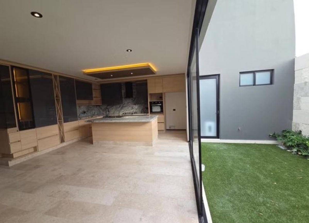 Cocina moderna con isla de madera, ventanal de cristal y patio con pasto sintético