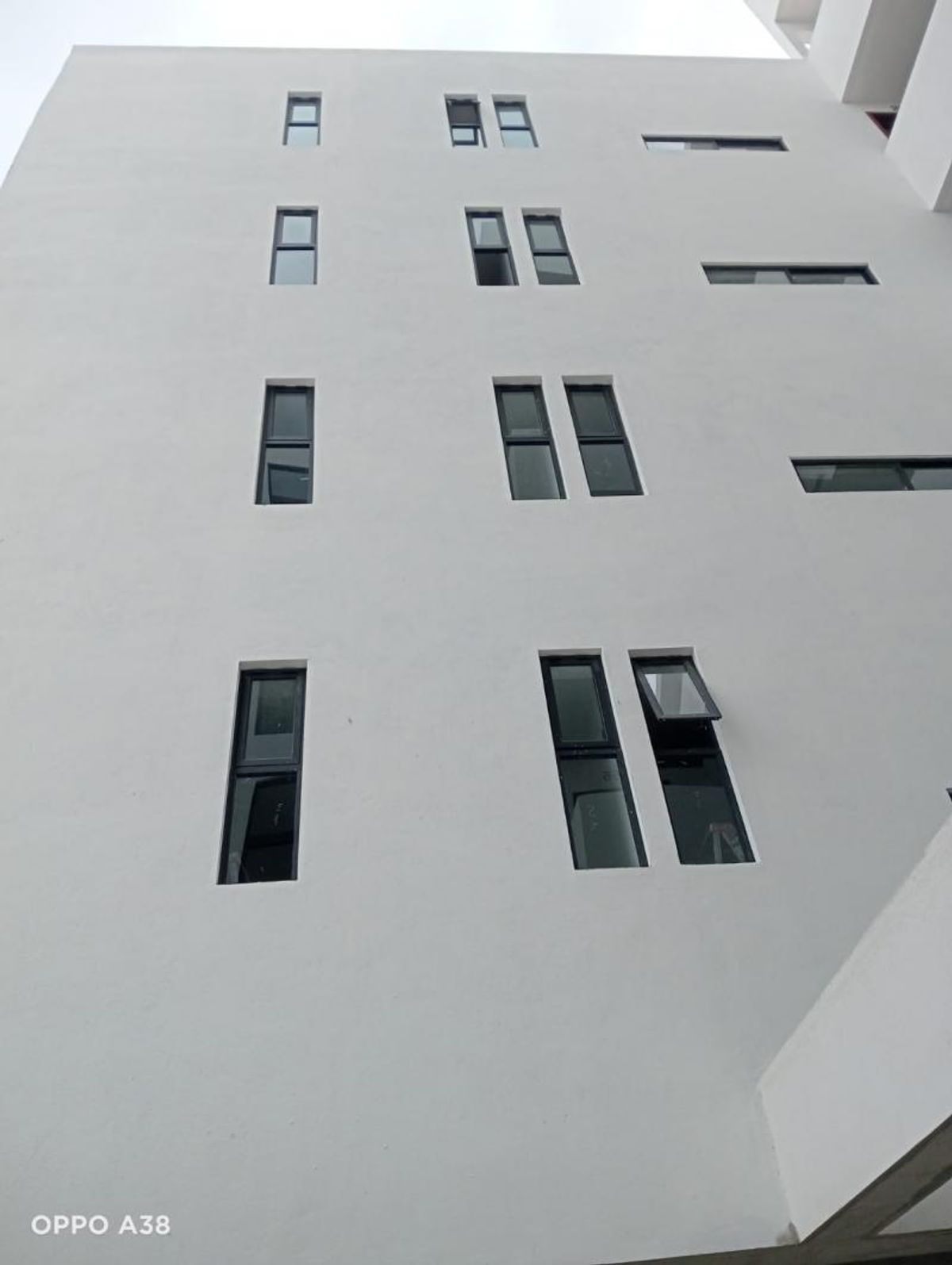 Fachada exterior de pared blanca con ventanas rectangulares de marcos oscuros en distintos niveles