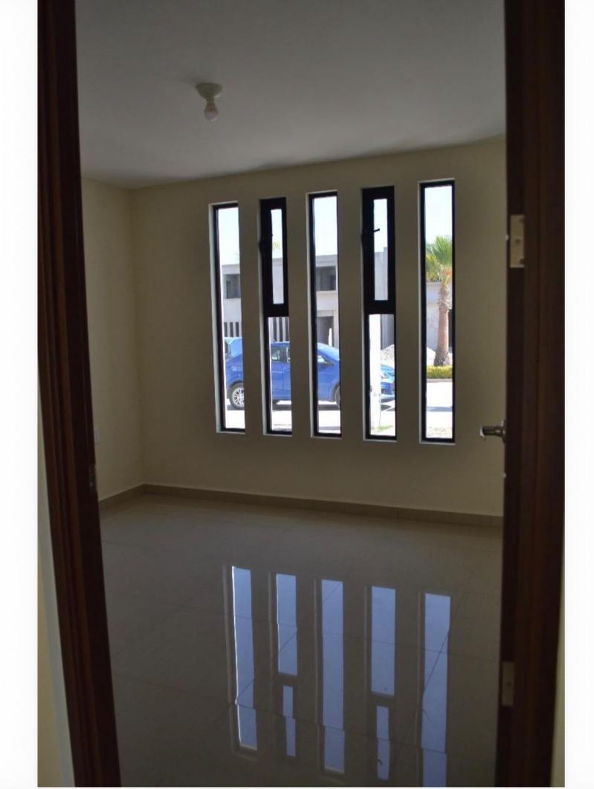 Habitación vacía con paredes claras, piso cerámico brillante y cinco ventanas verticales delgadas