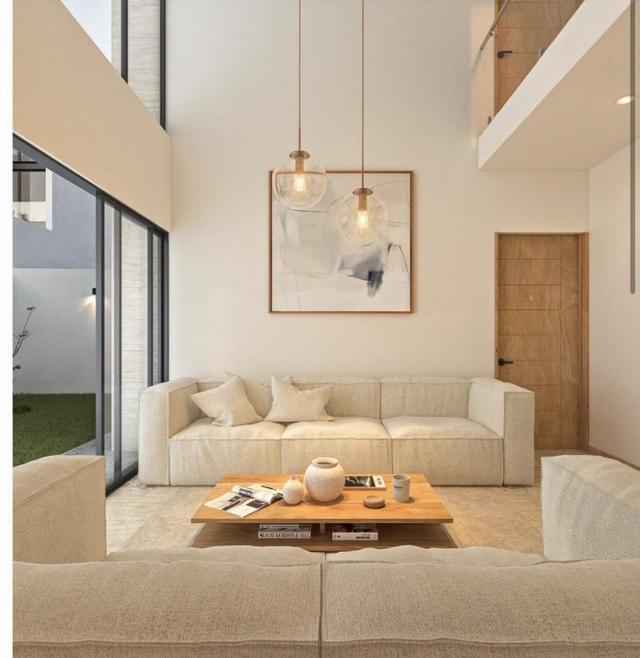 Sala de doble altura con sofás beige, mesa de centro de madera y ventanales