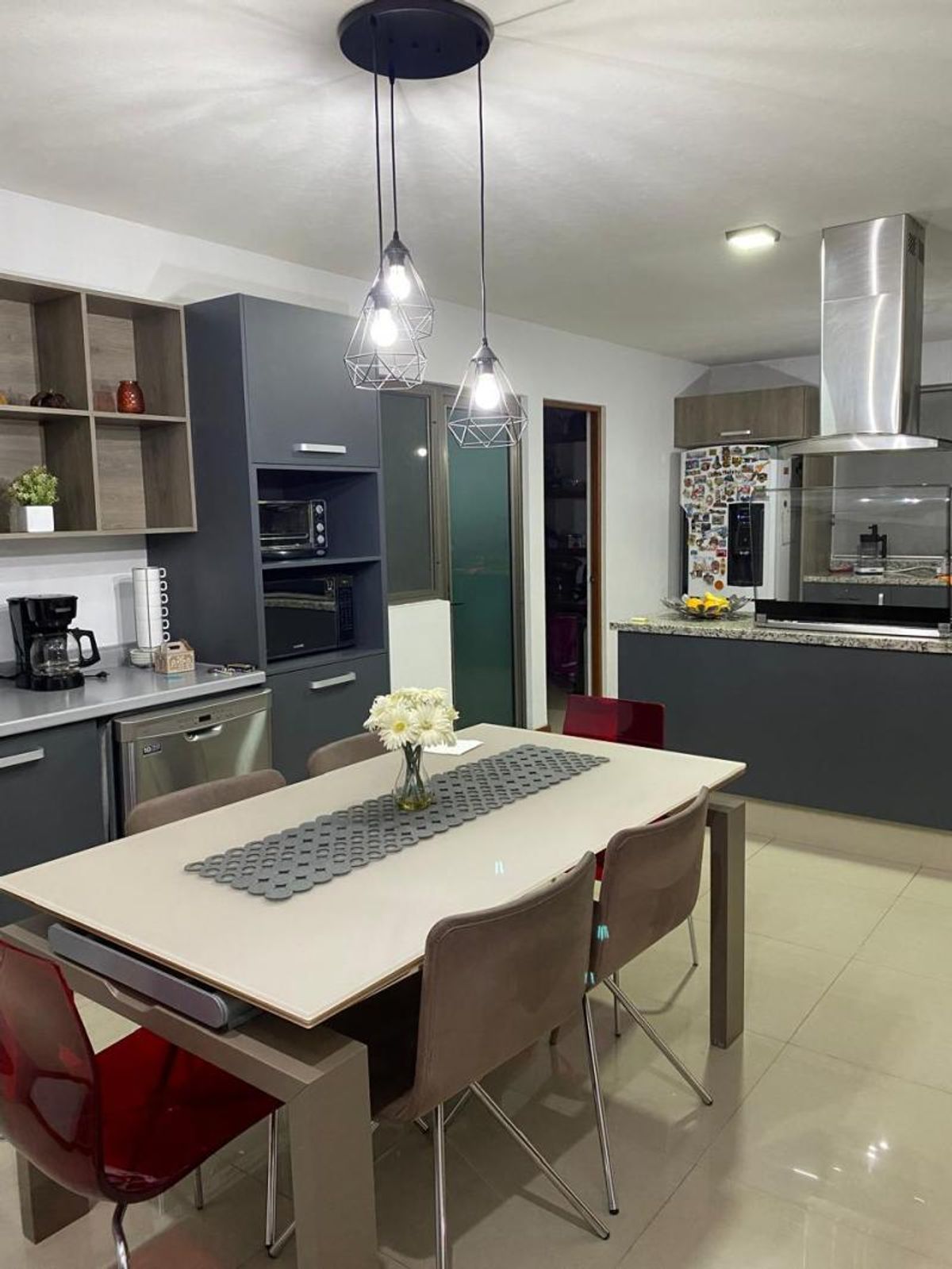 Comedor con lámparas colgantes junto a cocina con gabinetes grises y campana de acero