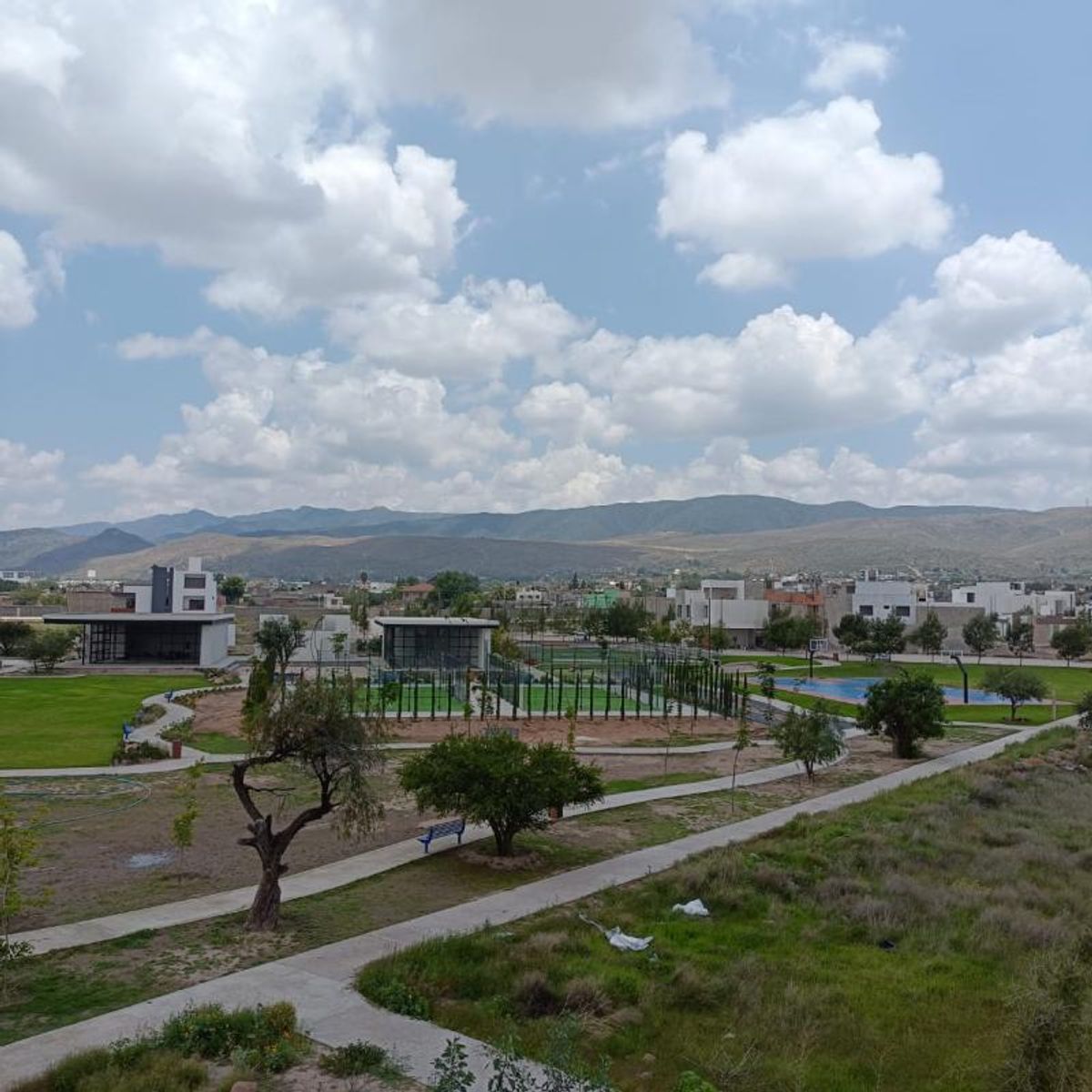 Área verde recreativa con caminos pavimentados, árboles, canchas deportivas y montañas al fondo