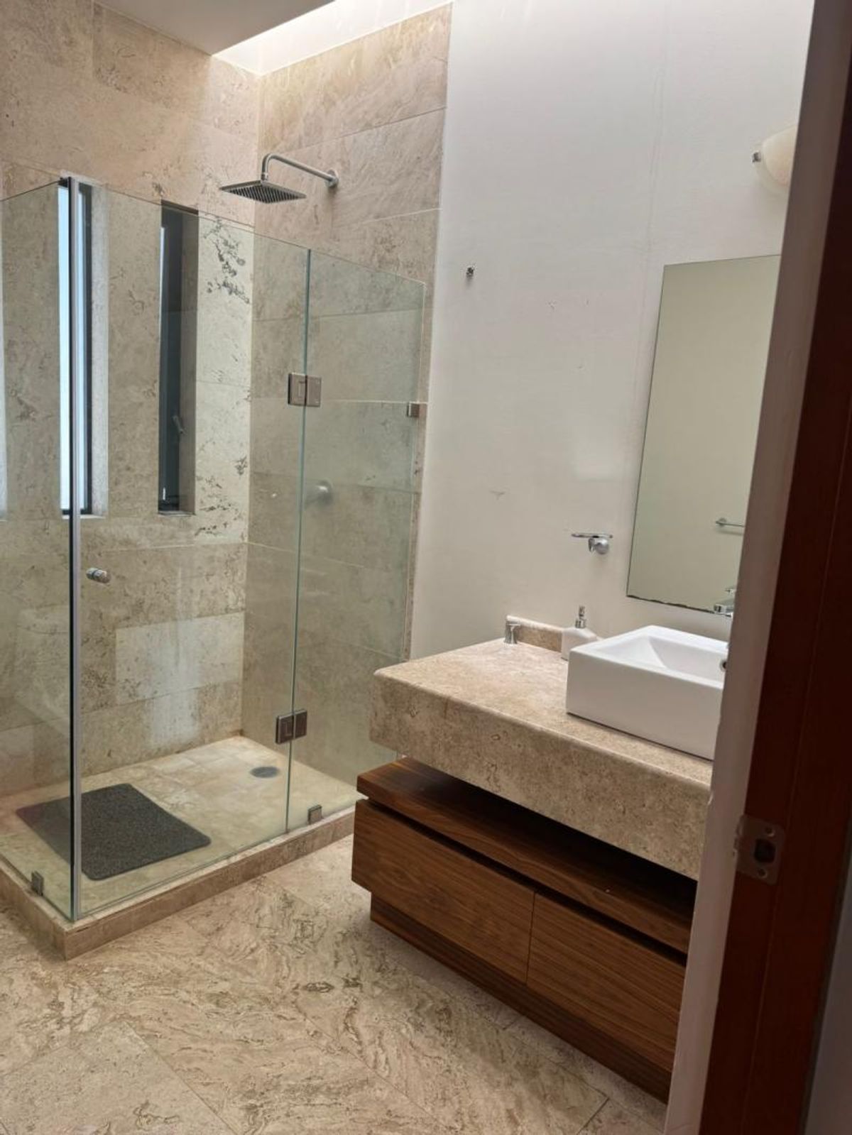 Baño con revestimiento de mármol, cancel de cristal y lavabo sobre mueble de madera