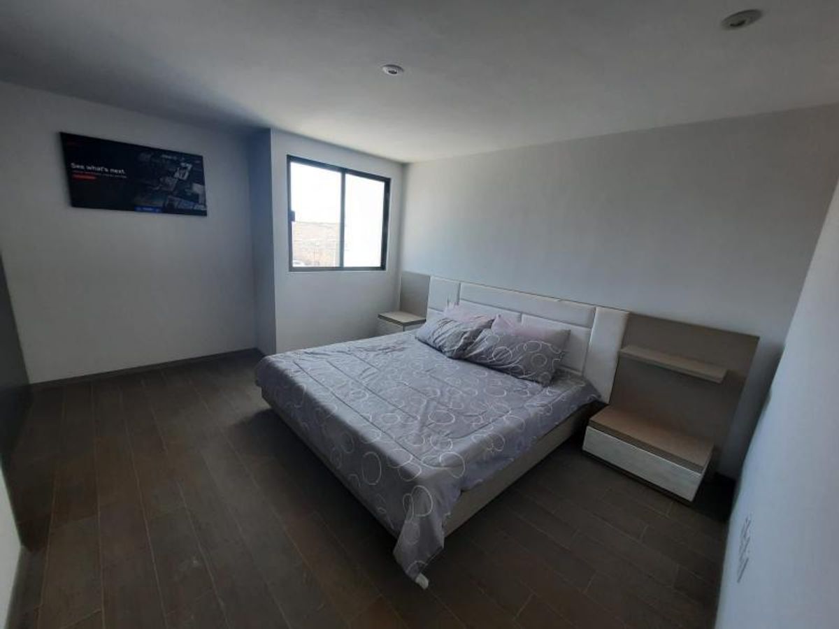 Recámara con cama, cabecera modular con burós integrados, ventana y piso tipo madera