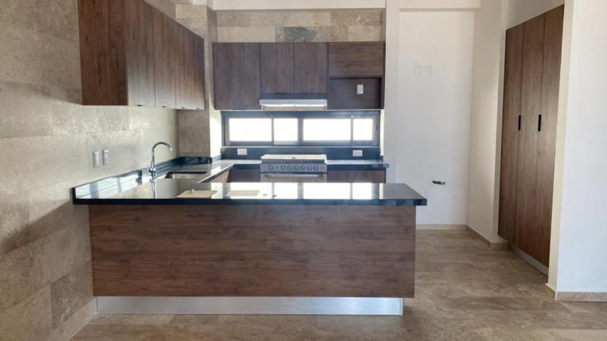 Cocina integral con barra de granito negro, gabinetes de madera y muro de azulejo beige