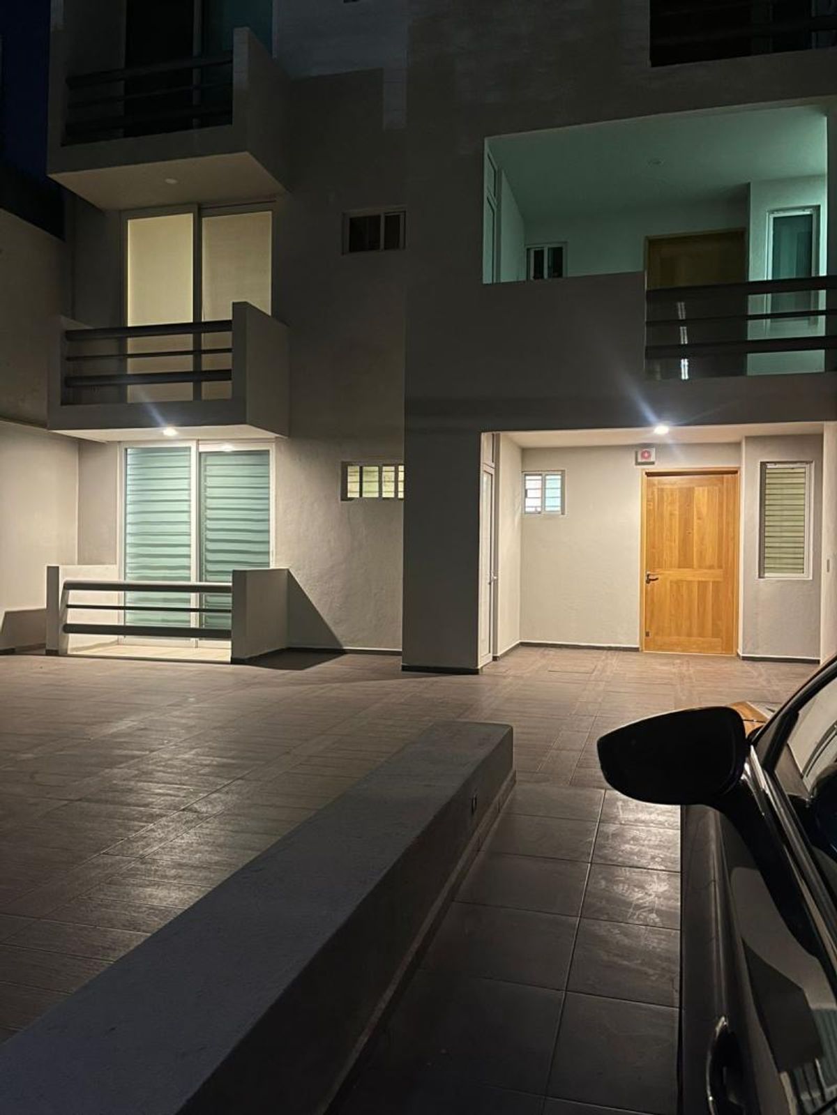Fachada exterior con patio azulejado, entrada con puerta de madera, balcones e iluminación nocturna