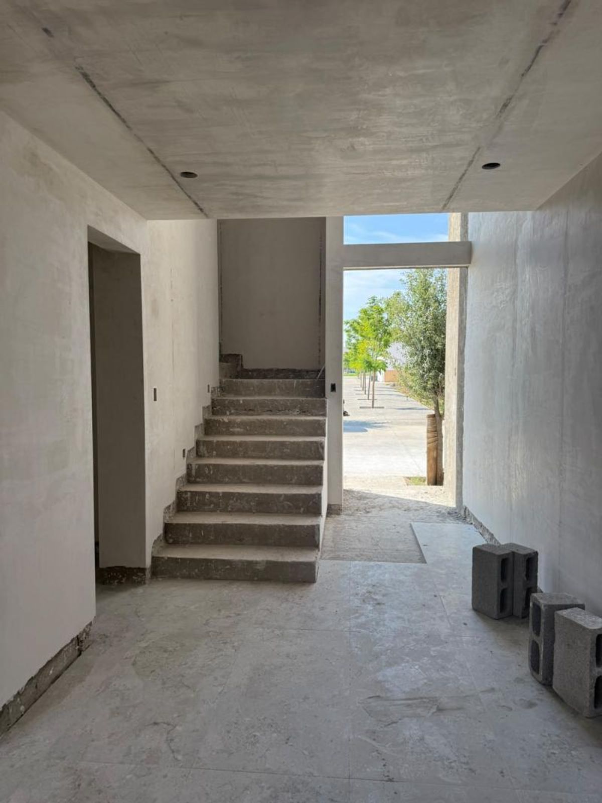 Interior en construcción con escaleras de concreto, muros aplanados y salida al exterior