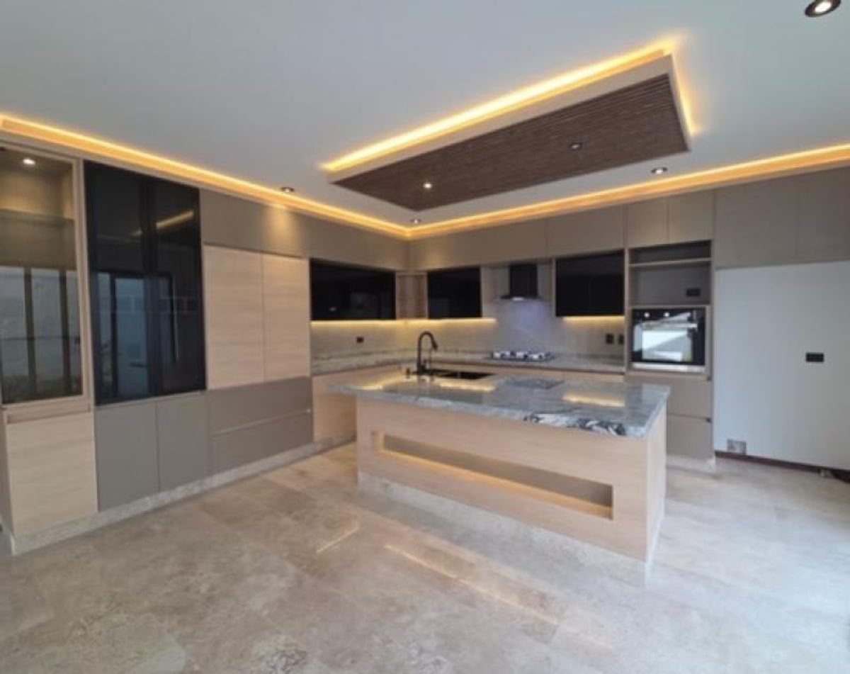 Cocina integral con isla central de mármol, gabinetes de madera e iluminación LED indirecta