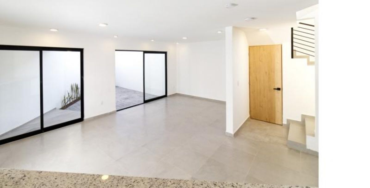 Sala con piso de porcelanato claro, ventanales corredizos negros, puerta de madera y escalera