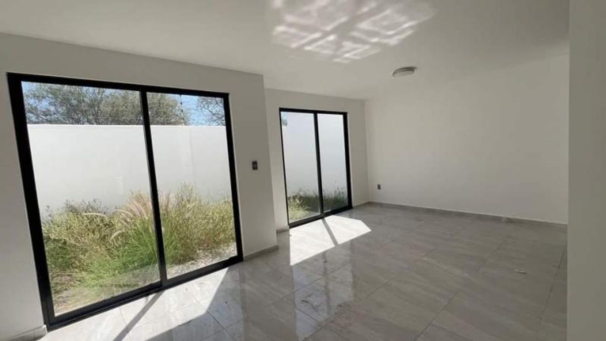 Habitación vacía con piso brillante, paredes blancas y grandes ventanales hacia el jardín