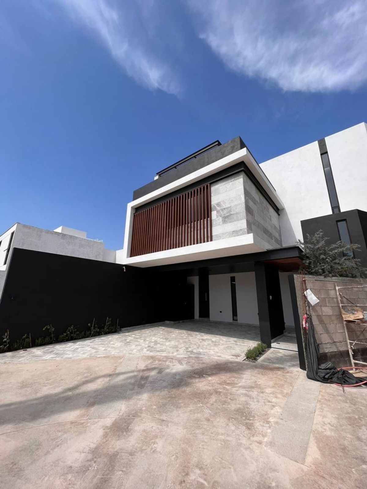 Fachada moderna de dos niveles con celosía de madera, revestimiento de piedra y cochera