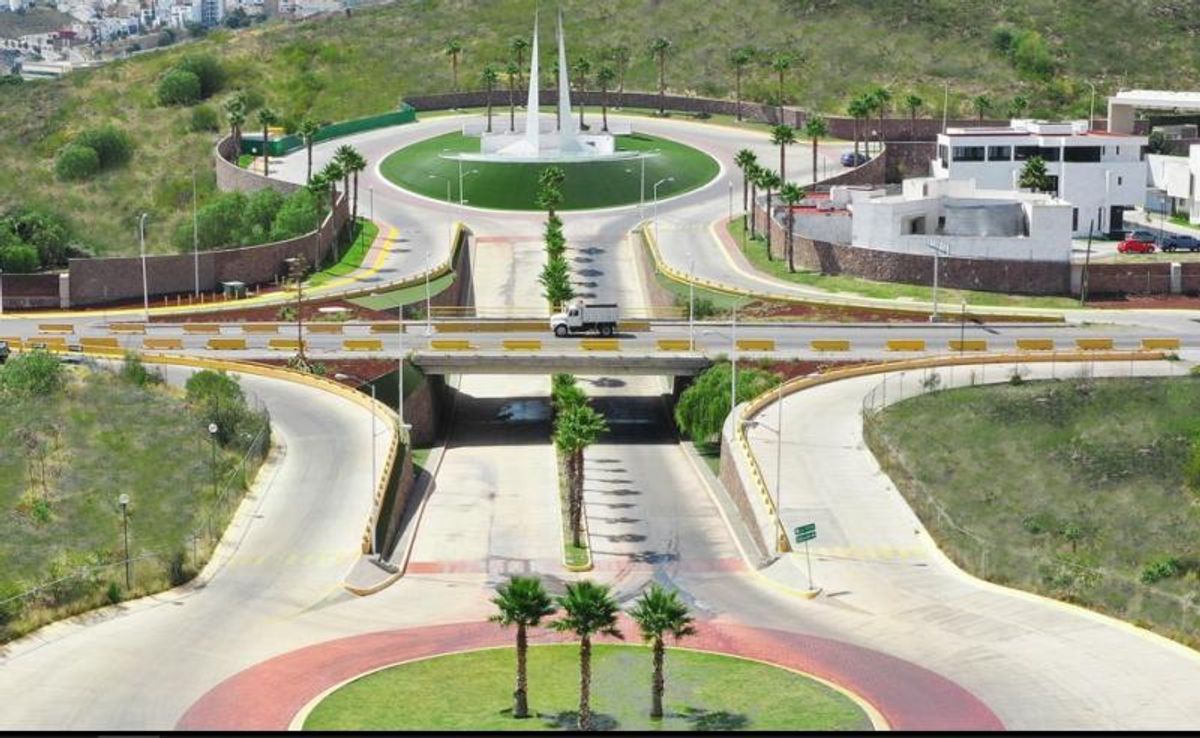 Glorieta de acceso con palmeras, puente elevado, camellones ajardinados y calles pavimentadas