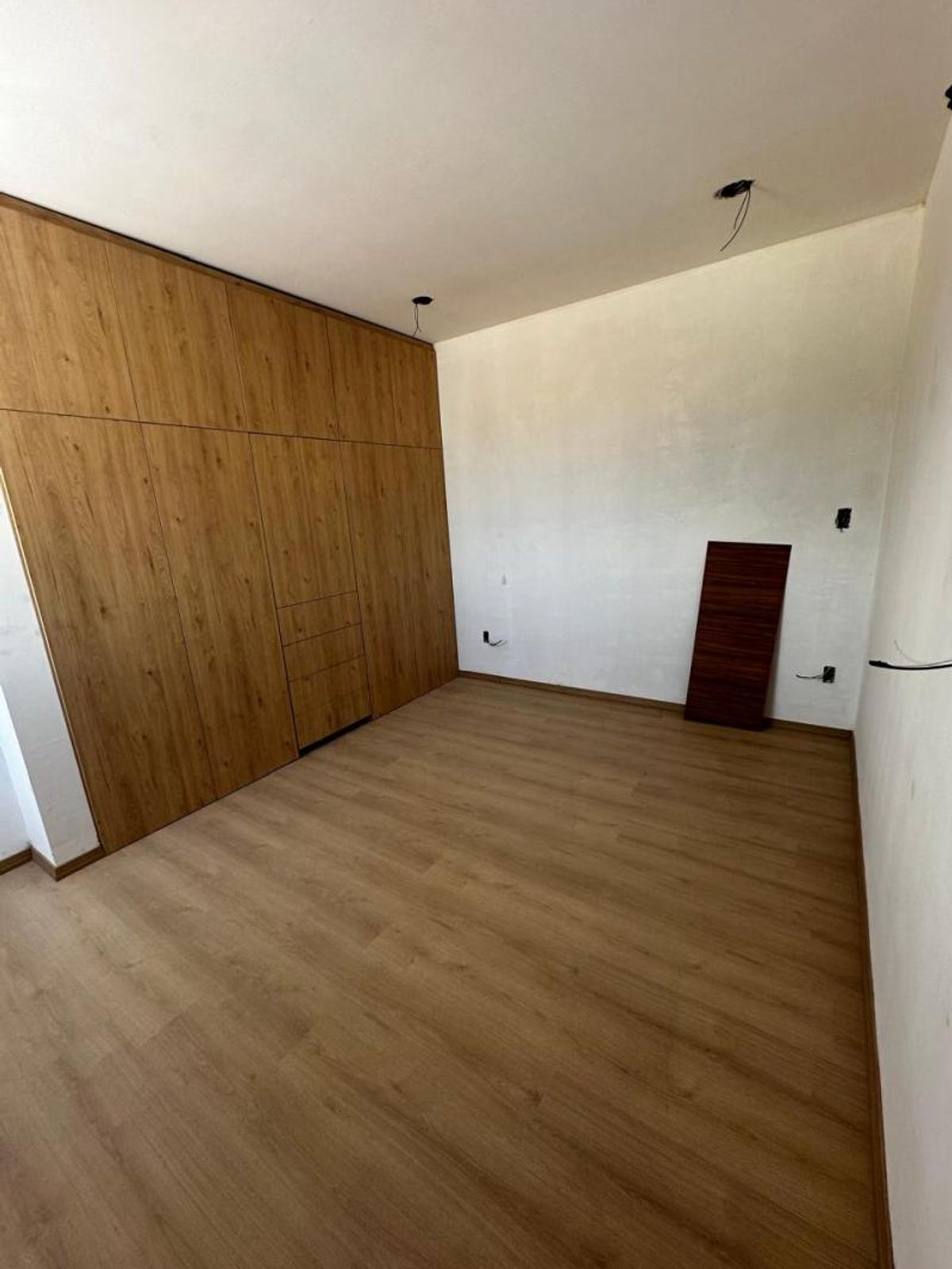 Habitación vacía con piso de madera, clóset empotrado de madera y paredes blancas