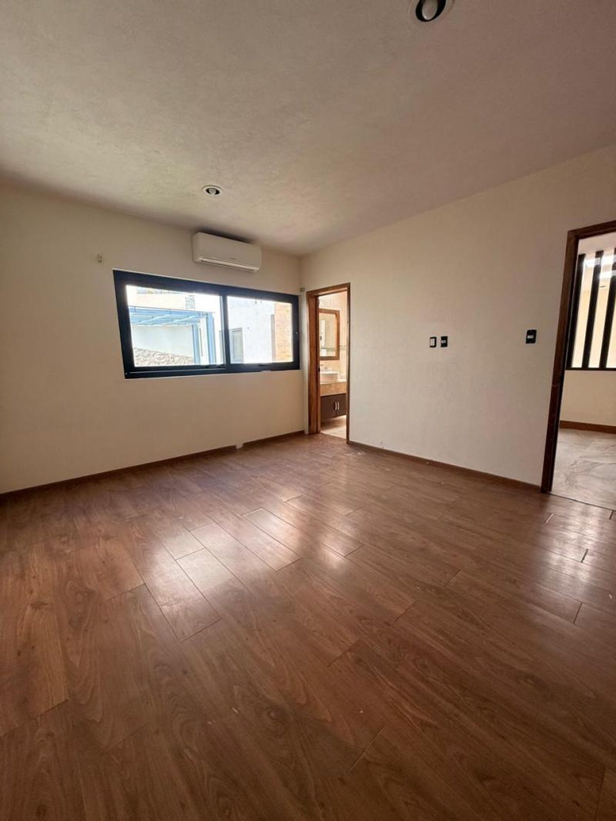 Habitación vacía con piso de madera, aire acondicionado y ventana con marco negro