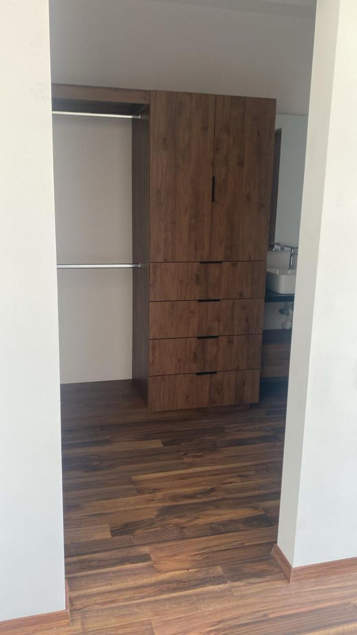 Vestidor con closet de madera oscura, cajones, barras para colgar y piso laminado