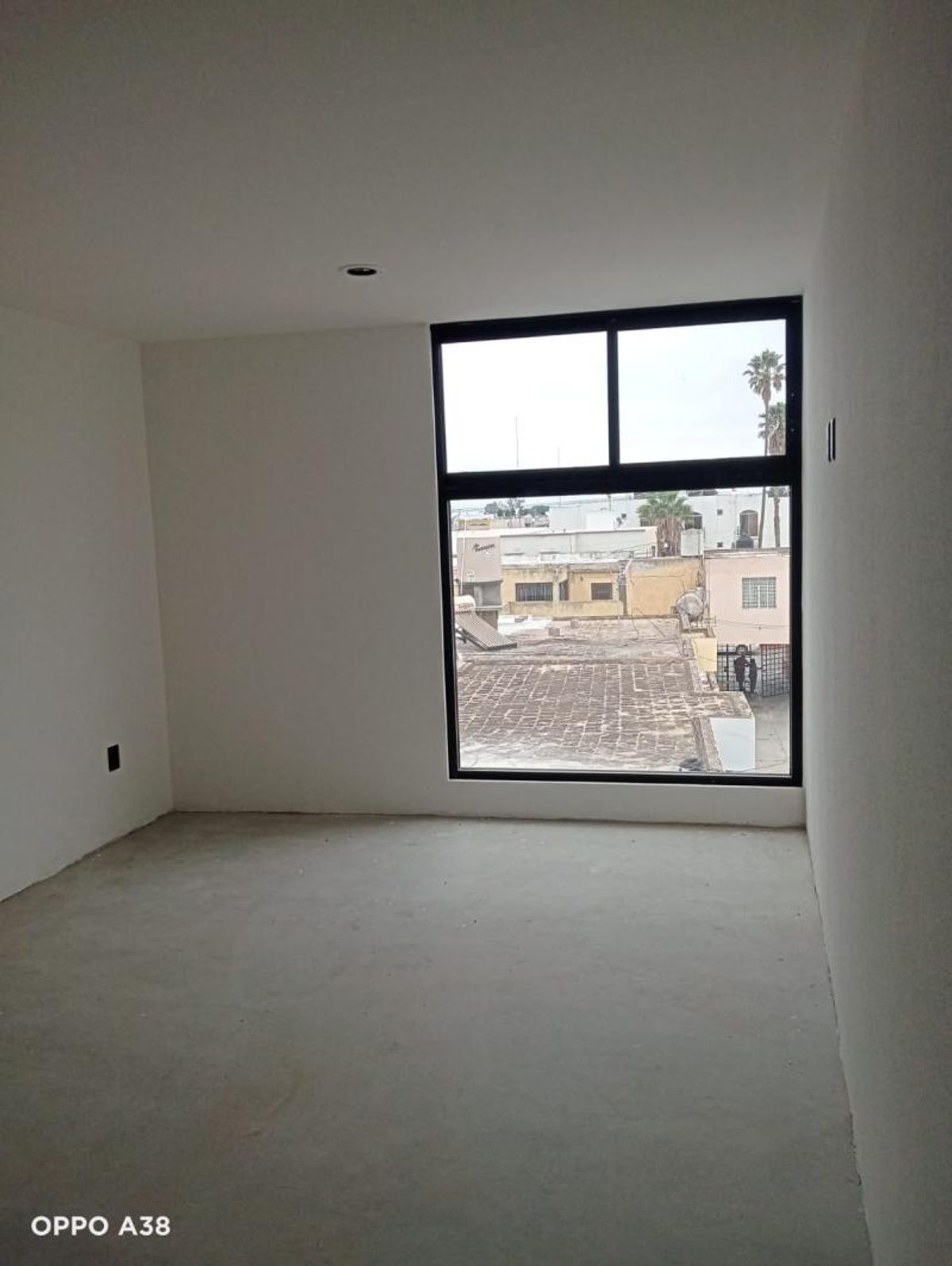 Habitación vacía con paredes blancas, piso de concreto y ventana grande de marco negro