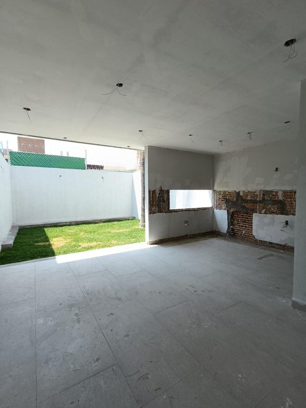 Área interior con piso de losetas grises y acceso a un jardín con césped