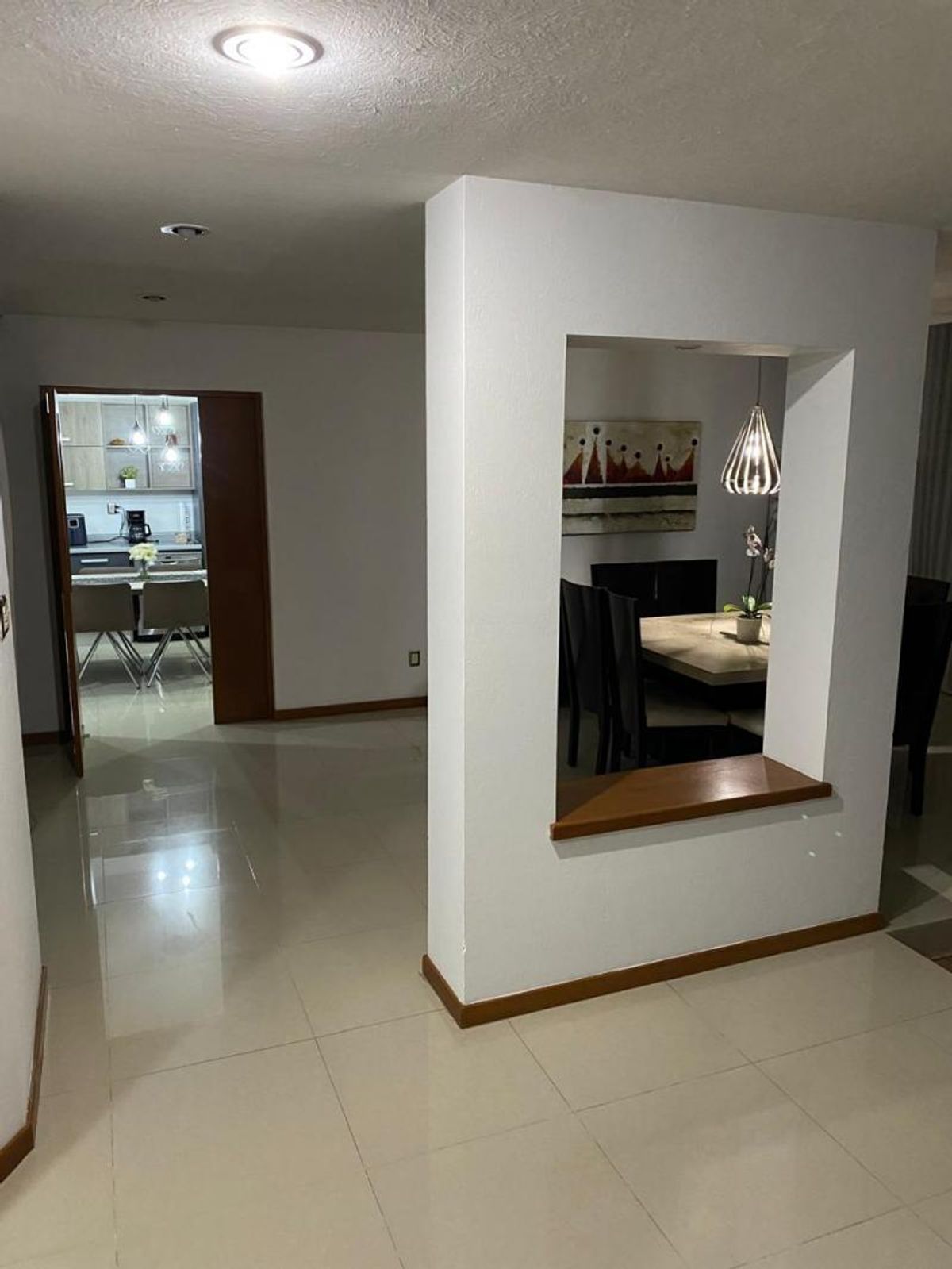 Pasillo con piso cerámico brillante, muro divisor con repisa y vista al comedor