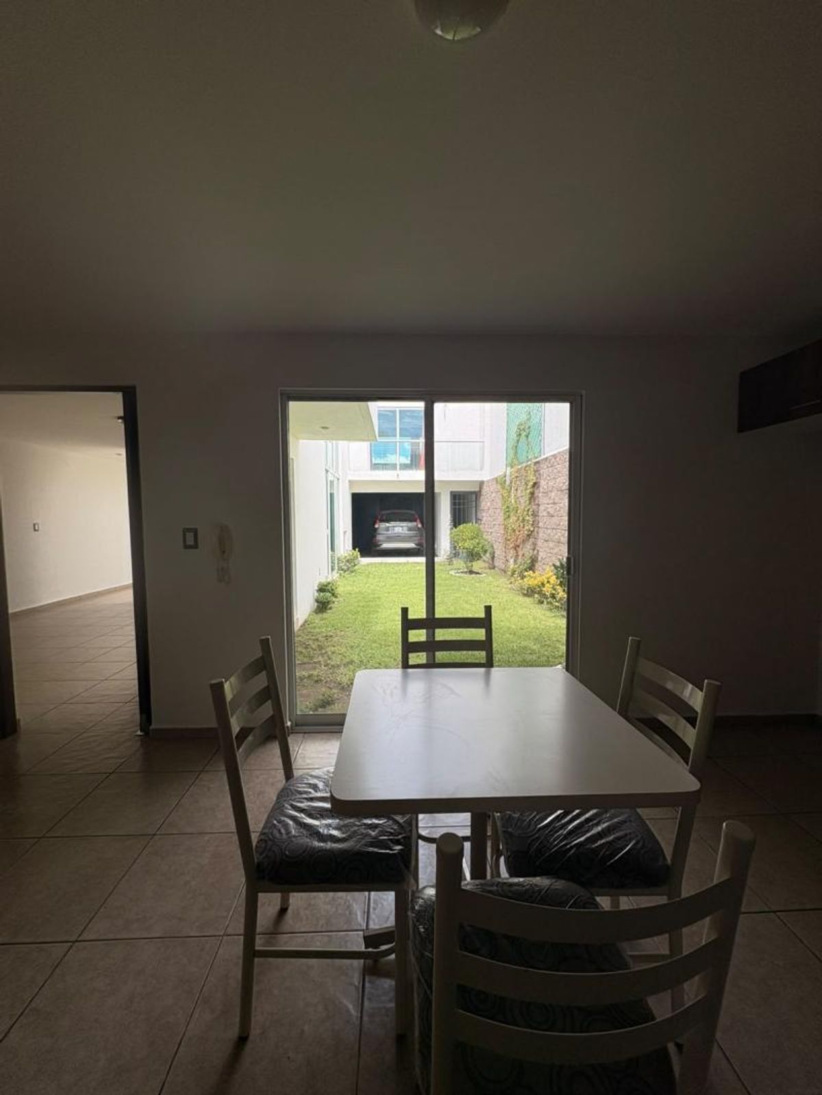 Comedor con mesa blanca y cuatro sillas frente a ventanal con vista al jardín