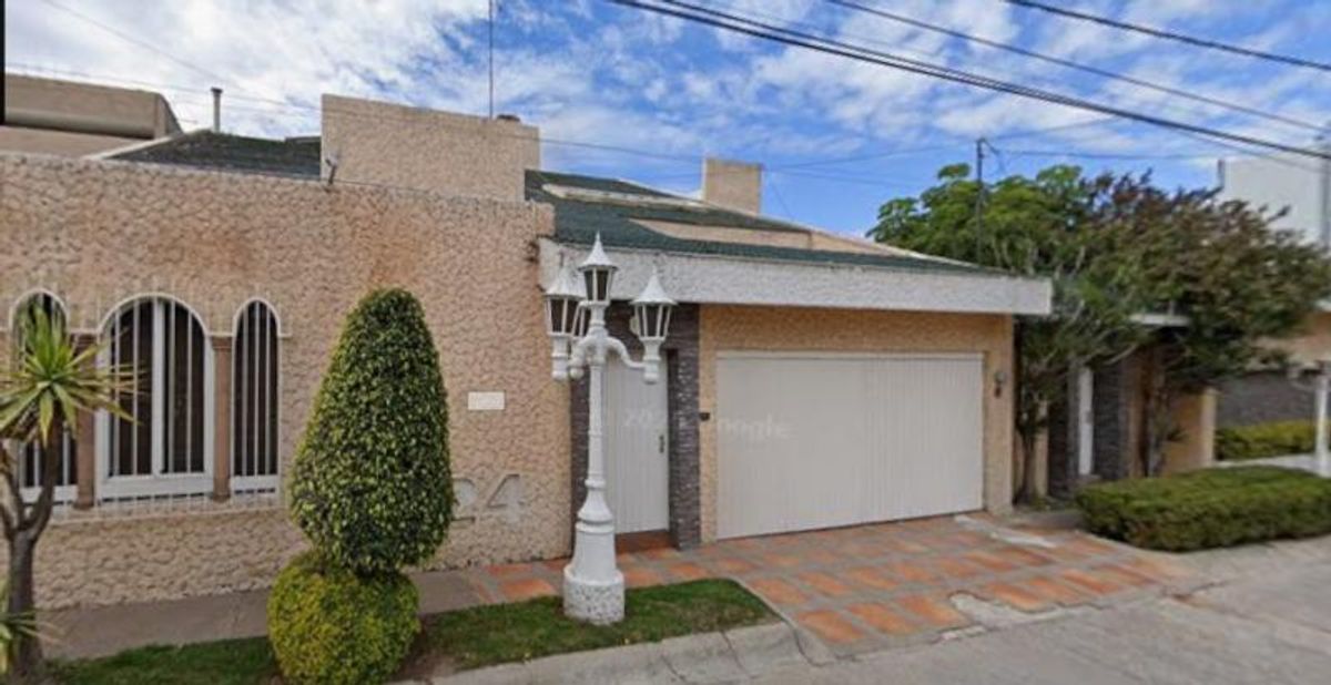 Fachada de casa con cochera blanca, farol clásico blanco, ventanas arqueadas y arbustos decorativos