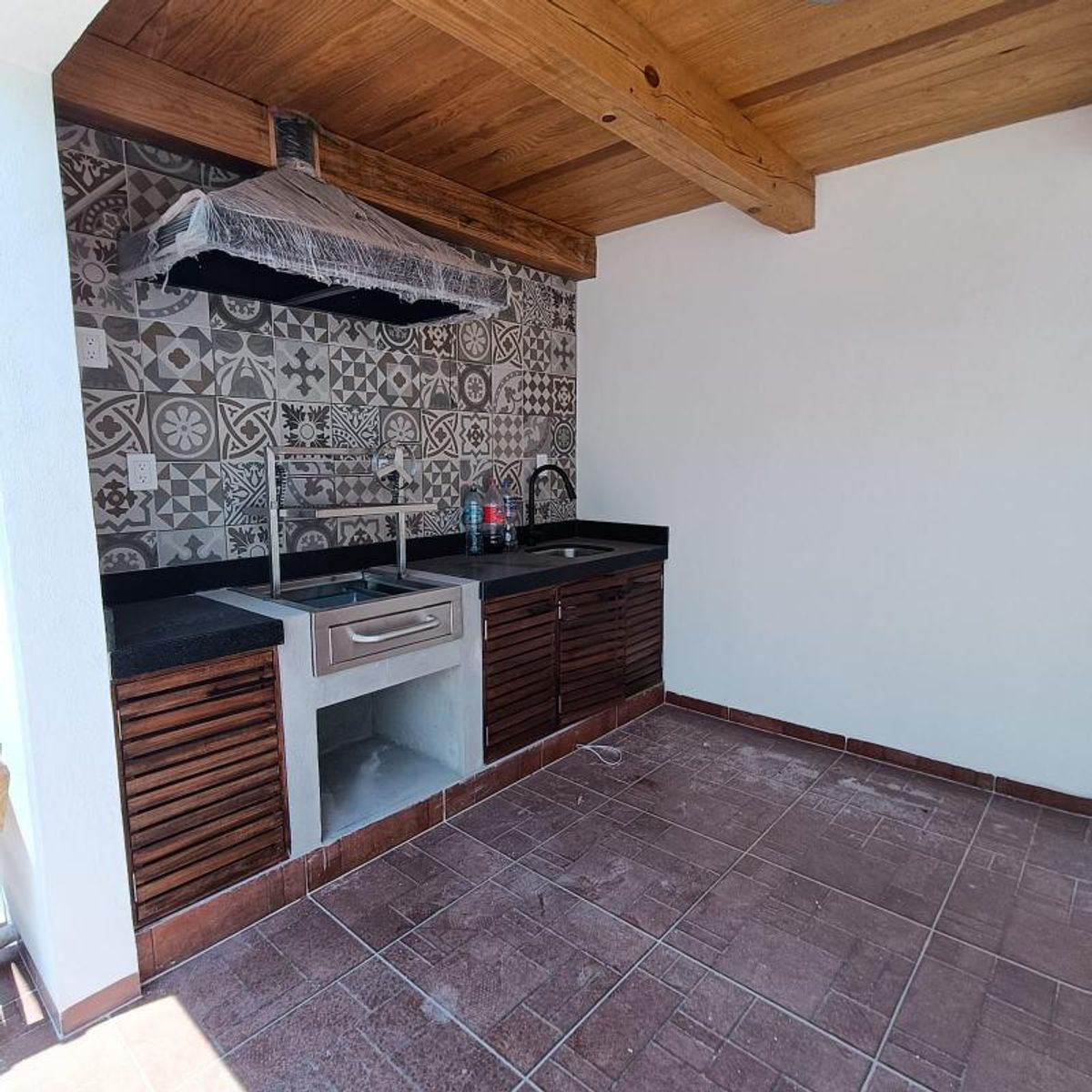 Área de asador con campana, azulejos decorativos, barra de granito negro y techo de madera