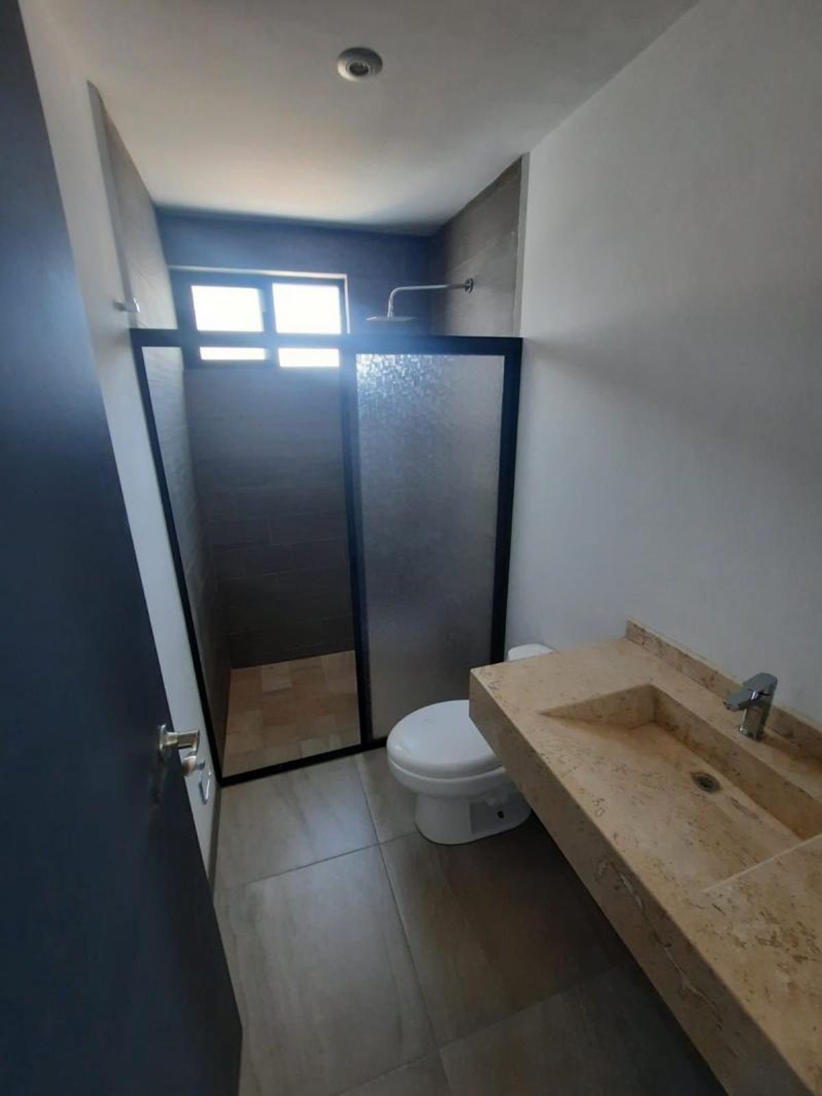 Baño con lavabo de mármol beige, inodoro blanco y regadera con cancelería negra esmerilada