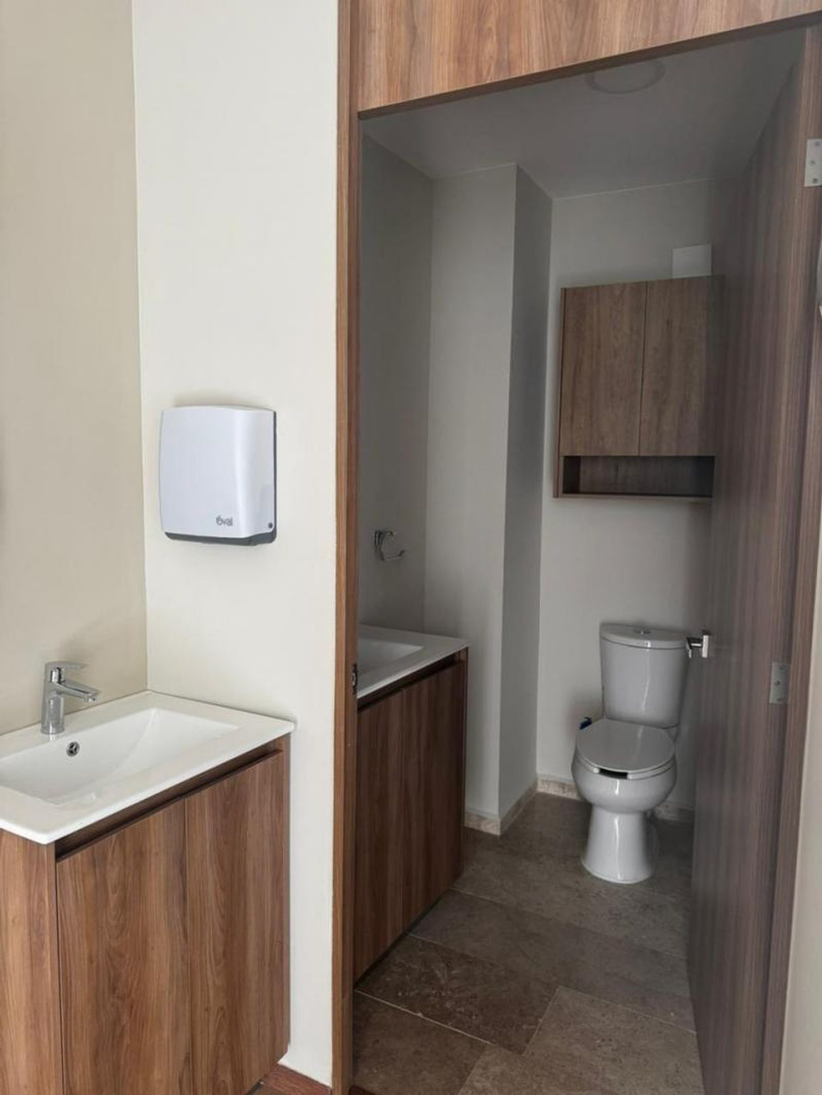 Lavabo con mueble de madera, despachador de toallas y acceso a baño con inodoro