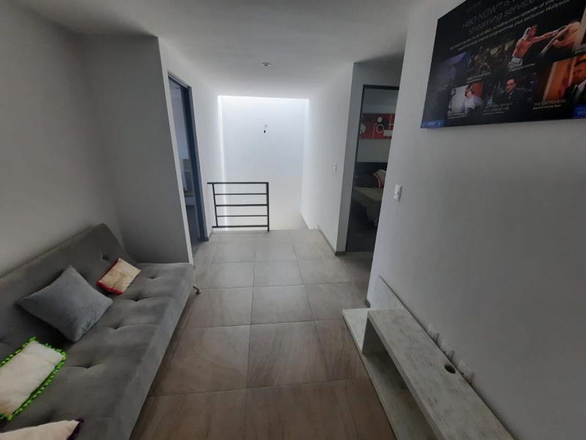 Área de estar con sofá gris, consola para televisión, piso de loseta y barandal metálico
