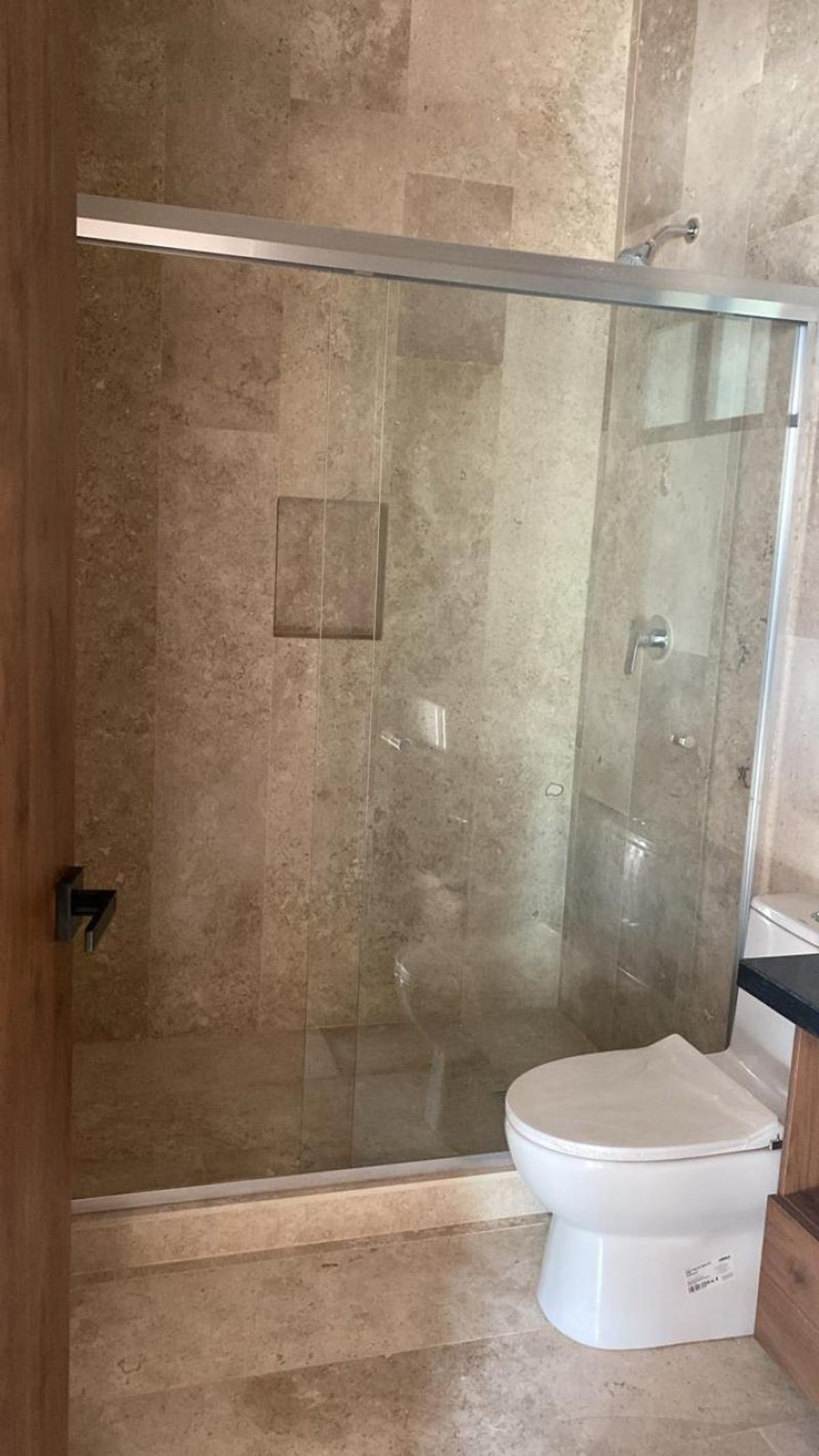 Baño con cancel de cristal en regadera, paredes de azulejo beige e inodoro blanco