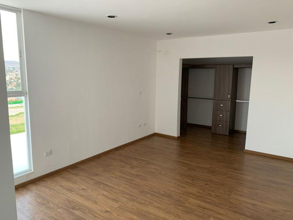 Habitación vacía con piso laminado de madera, paredes blancas, ventanal y vestidor de madera