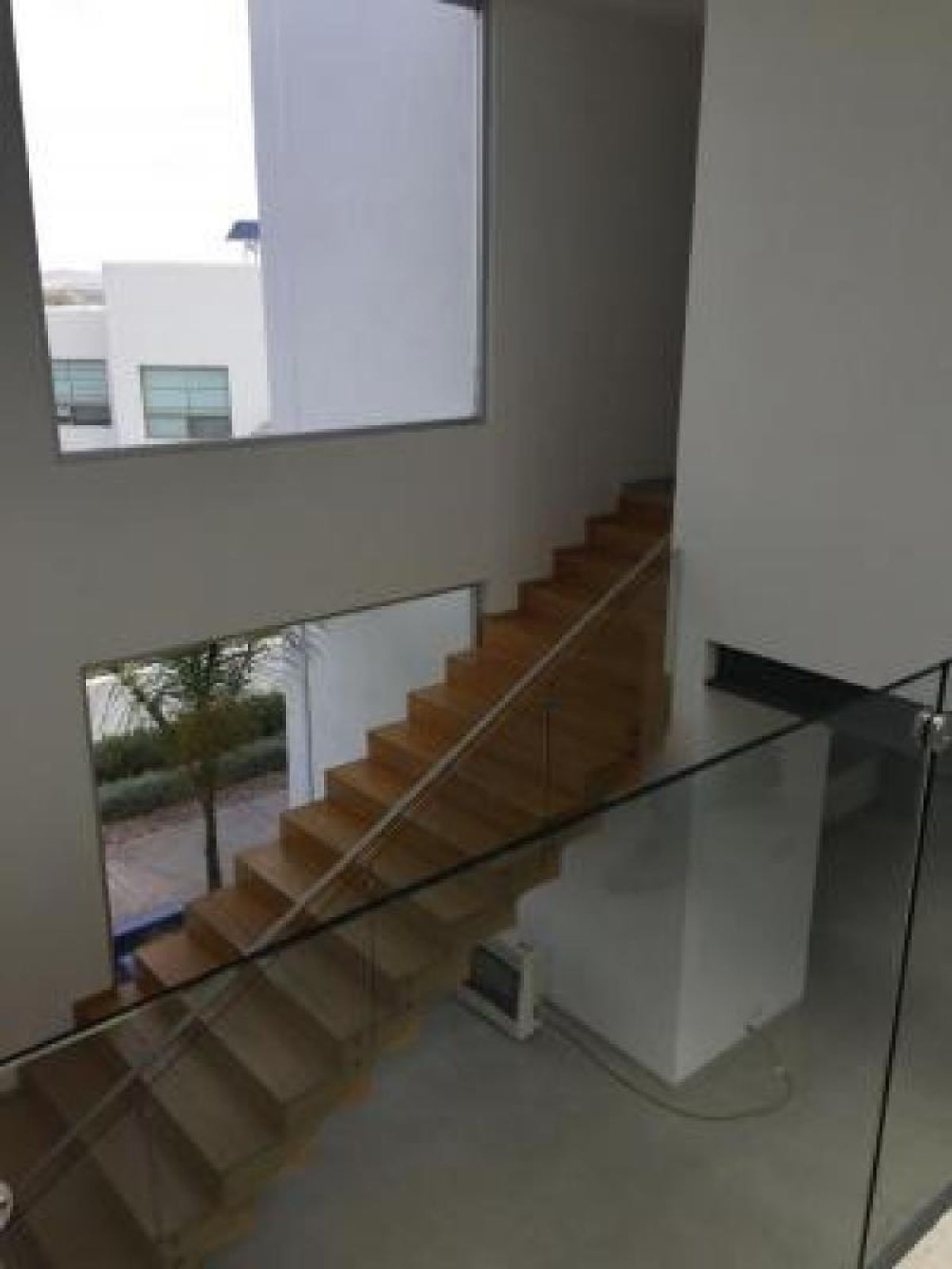 Escalera de madera con barandal de cristal y ventanales en espacio de doble altura