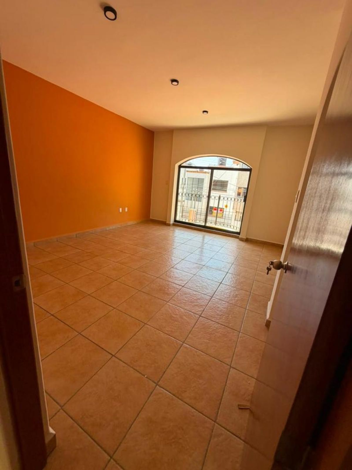 Habitación vacía con piso de cerámica terracota, pared naranja y ventanal arqueado al fondo