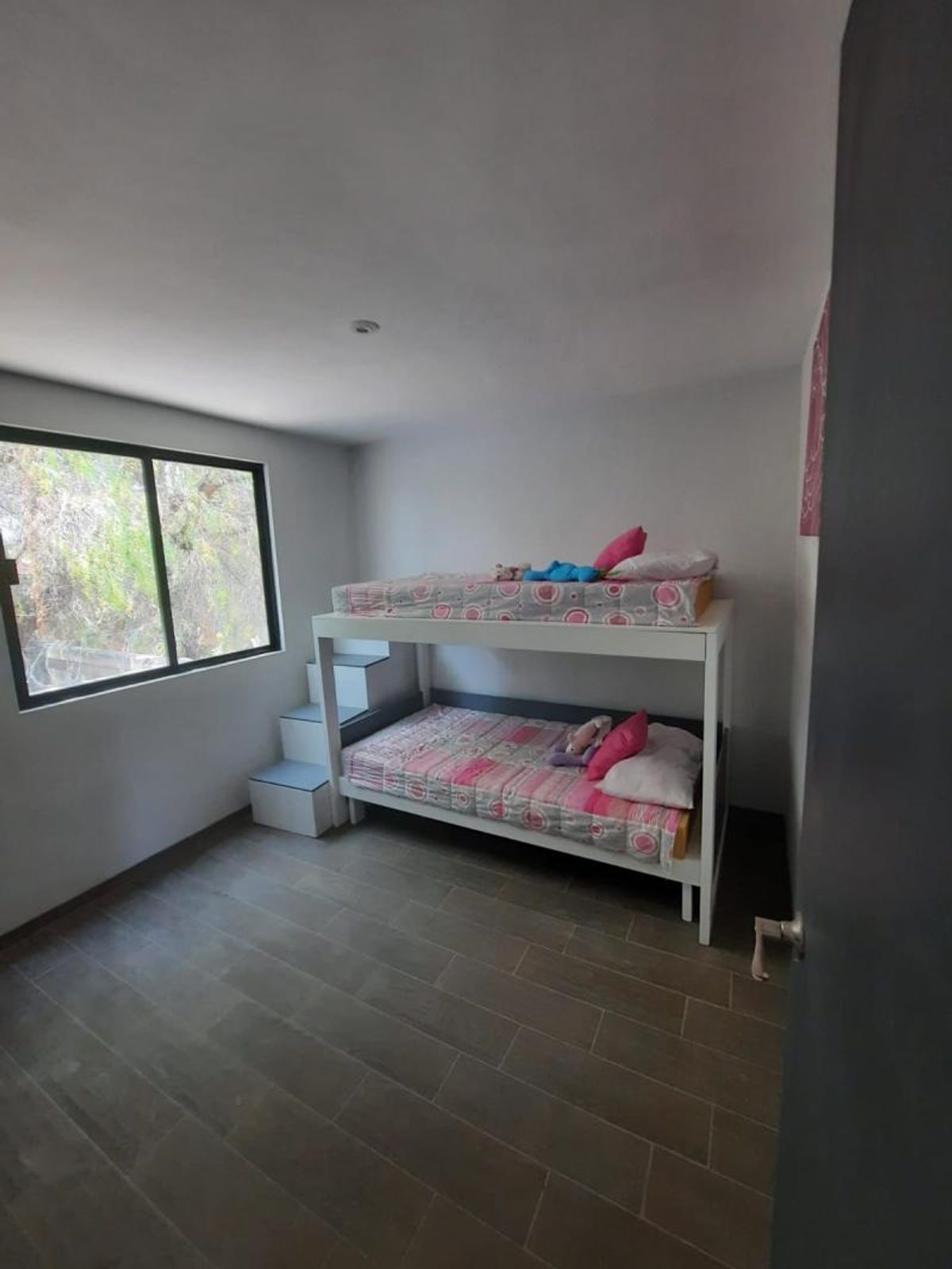 Recámara con litera blanca con escalones integrados, piso tipo madera y ventana rectangular