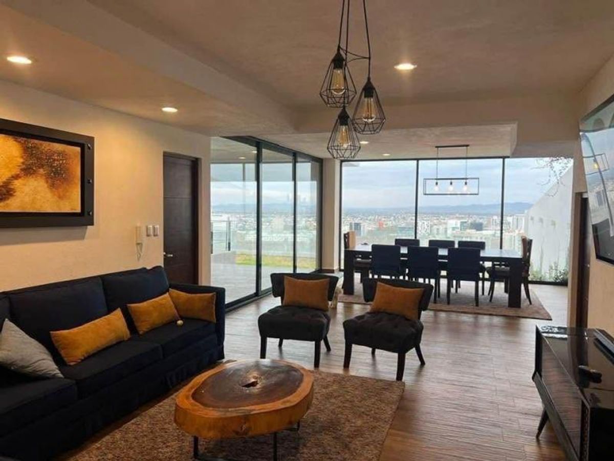 Sala con sofá azul, mesa de centro de madera y comedor frente a ventanales