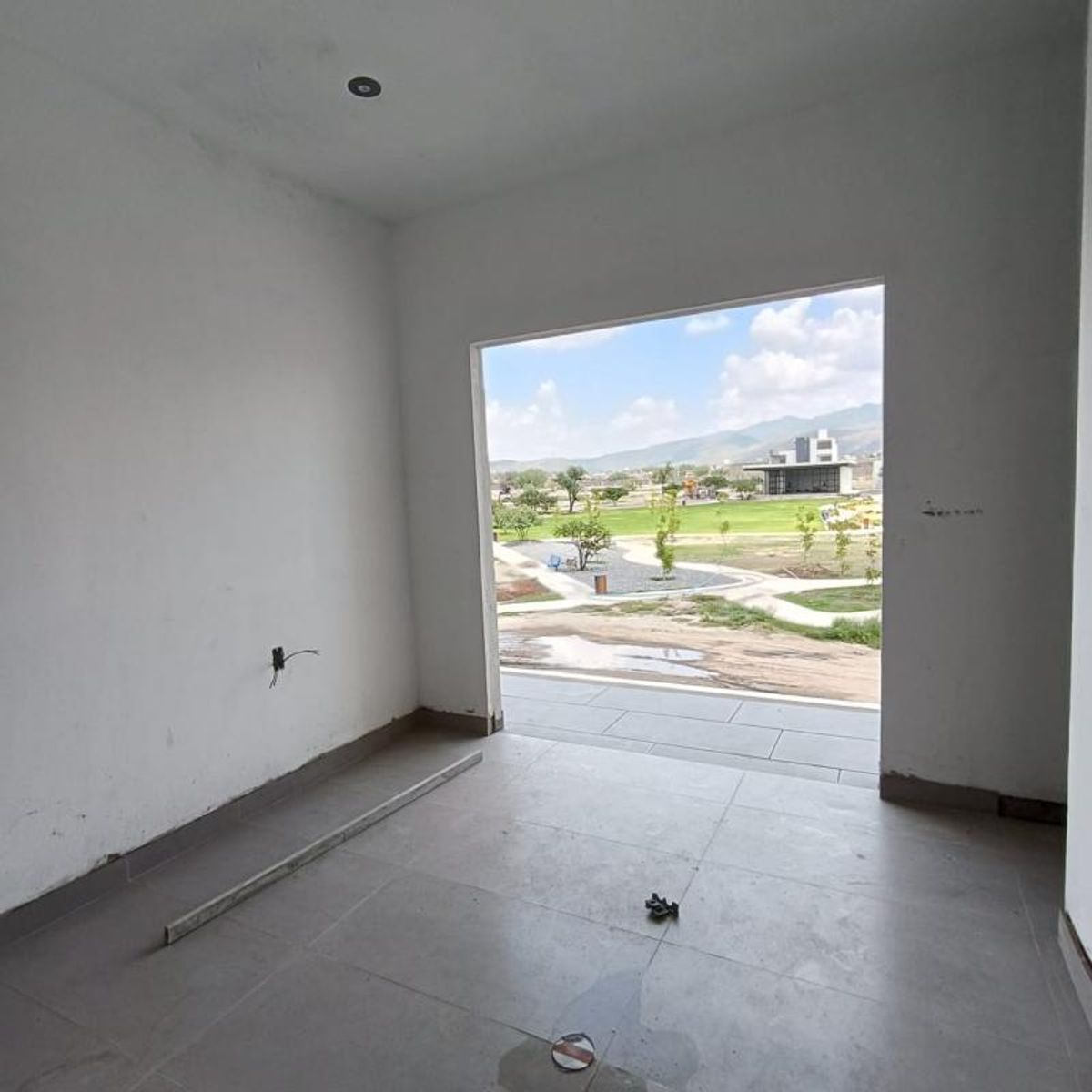 Habitación vacía con paredes blancas, piso gris y amplio acceso hacia el área verde