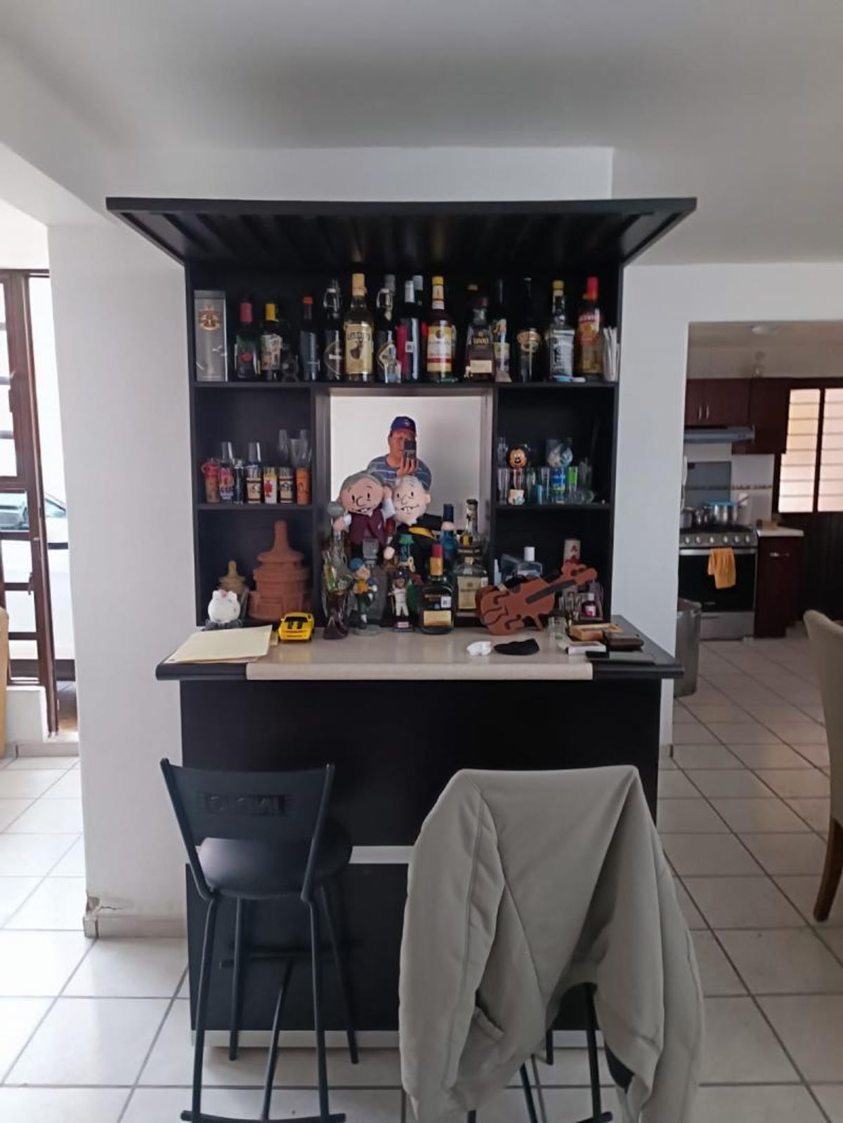 Mueble de bar de madera oscura con repisas para botellas, barra y bancos altos