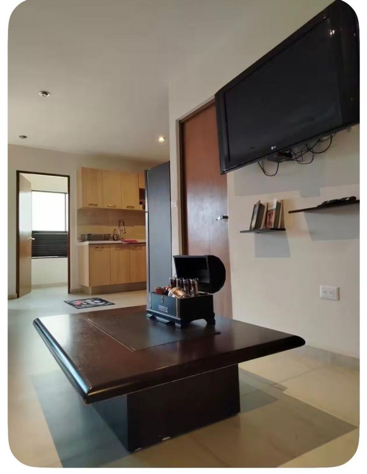 Sala con mesa de madera oscura, televisión montada en pared y cocina de madera al fondo
