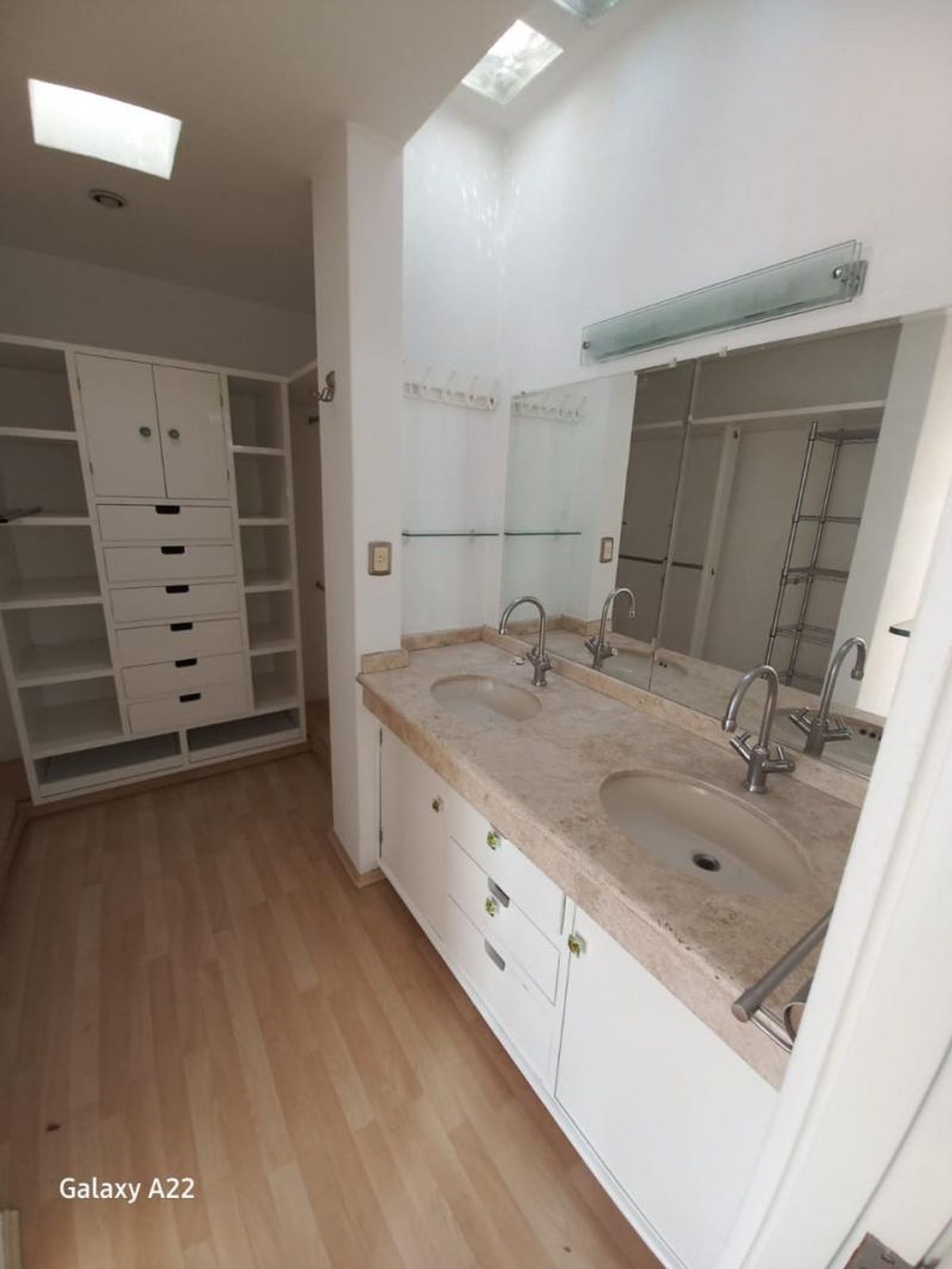 Doble lavabo con cubierta de mármol beige, gabinetes blancos, espejo y mueble de vestidor