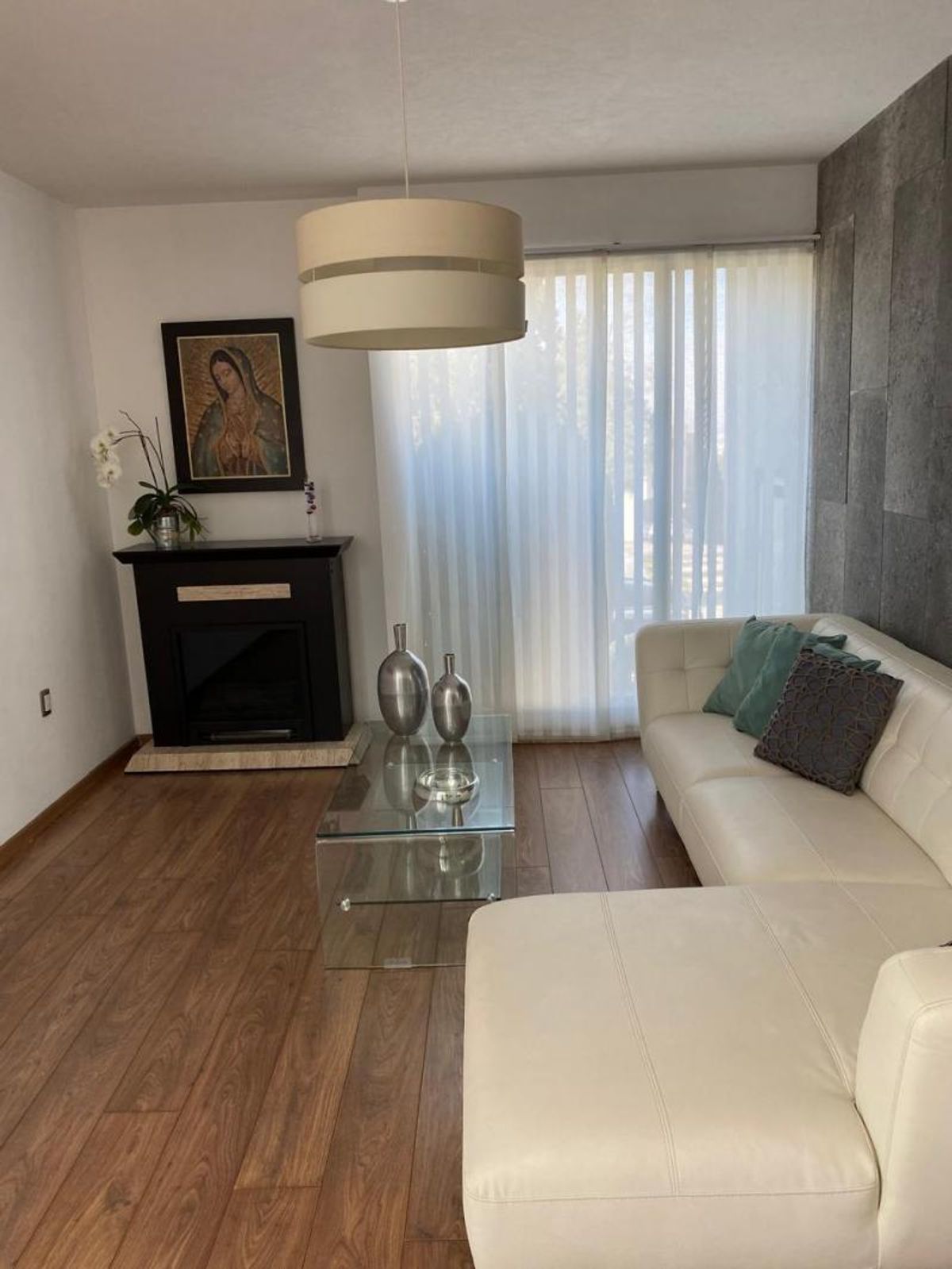 Sala con sofá modular blanco, mesa de cristal, chimenea oscura y piso laminado