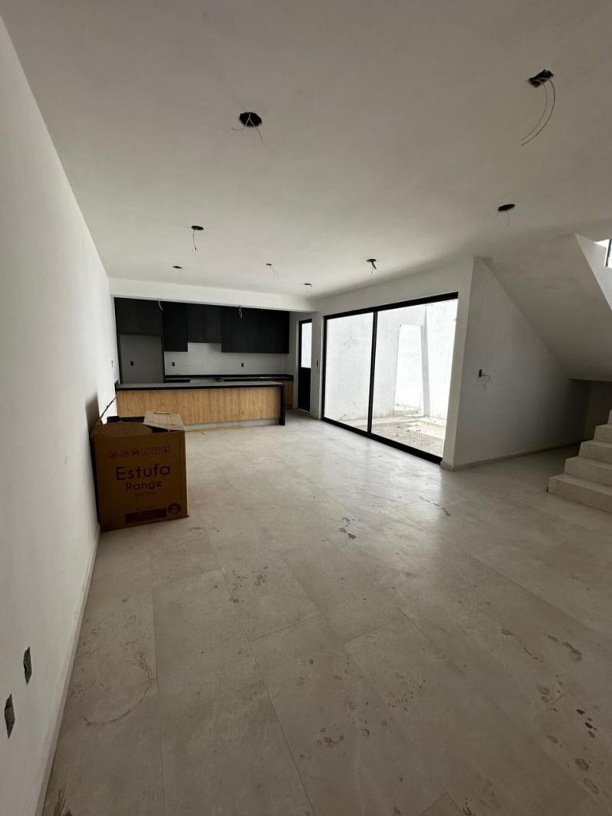 Espacio abierto con piso claro, cocina de gabinetes negros al fondo y ventanales corredizos