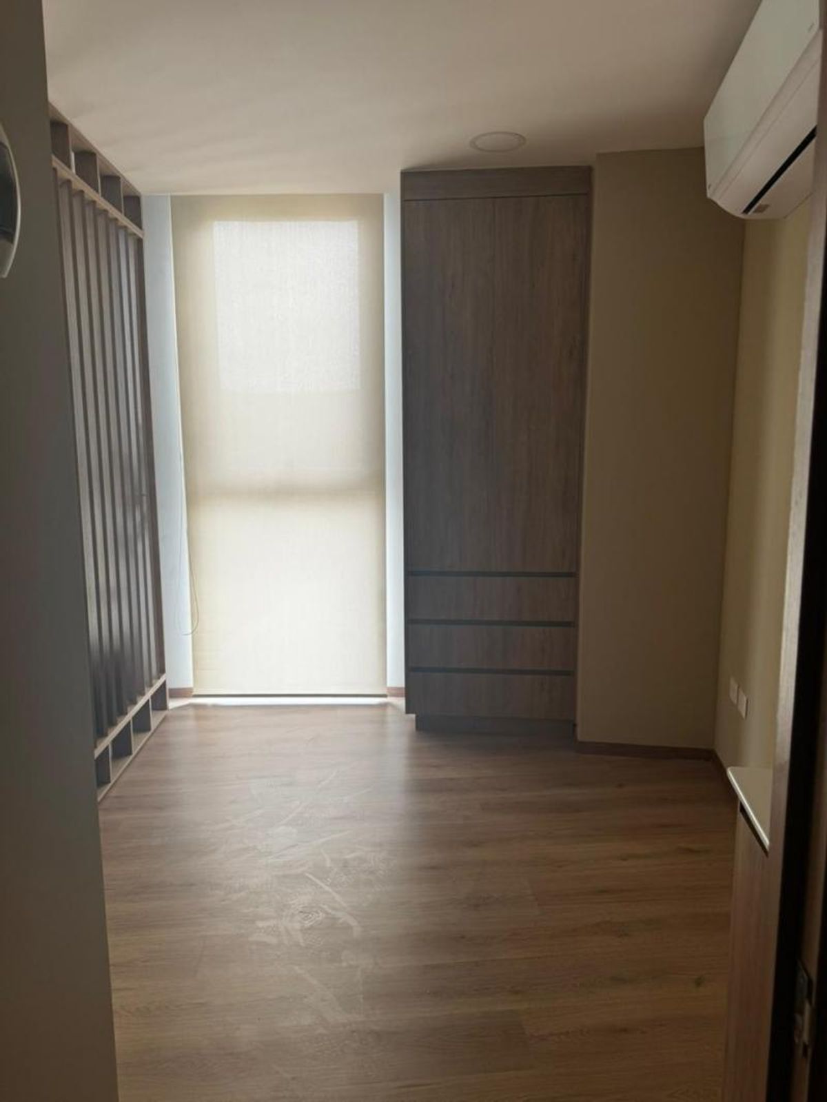 Consultorio vacío con piso laminado de madera, ventana con persiana enrollable y armario empotrado